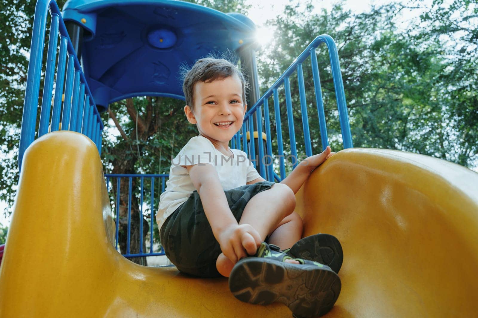 happy preschooler boy playing on a slide on the playground in summer