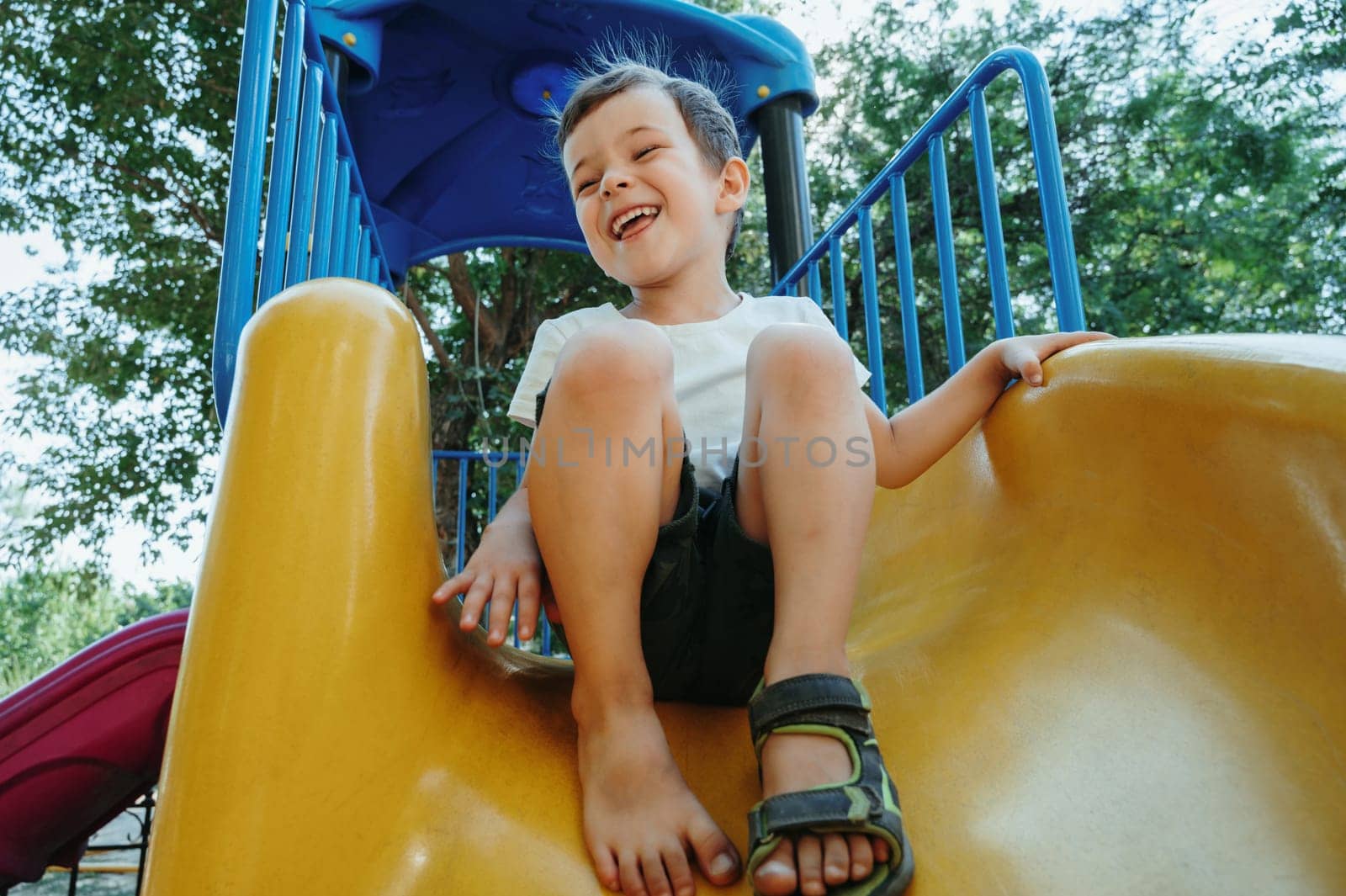 happy preschooler boy playing on a slide on the playground in summer