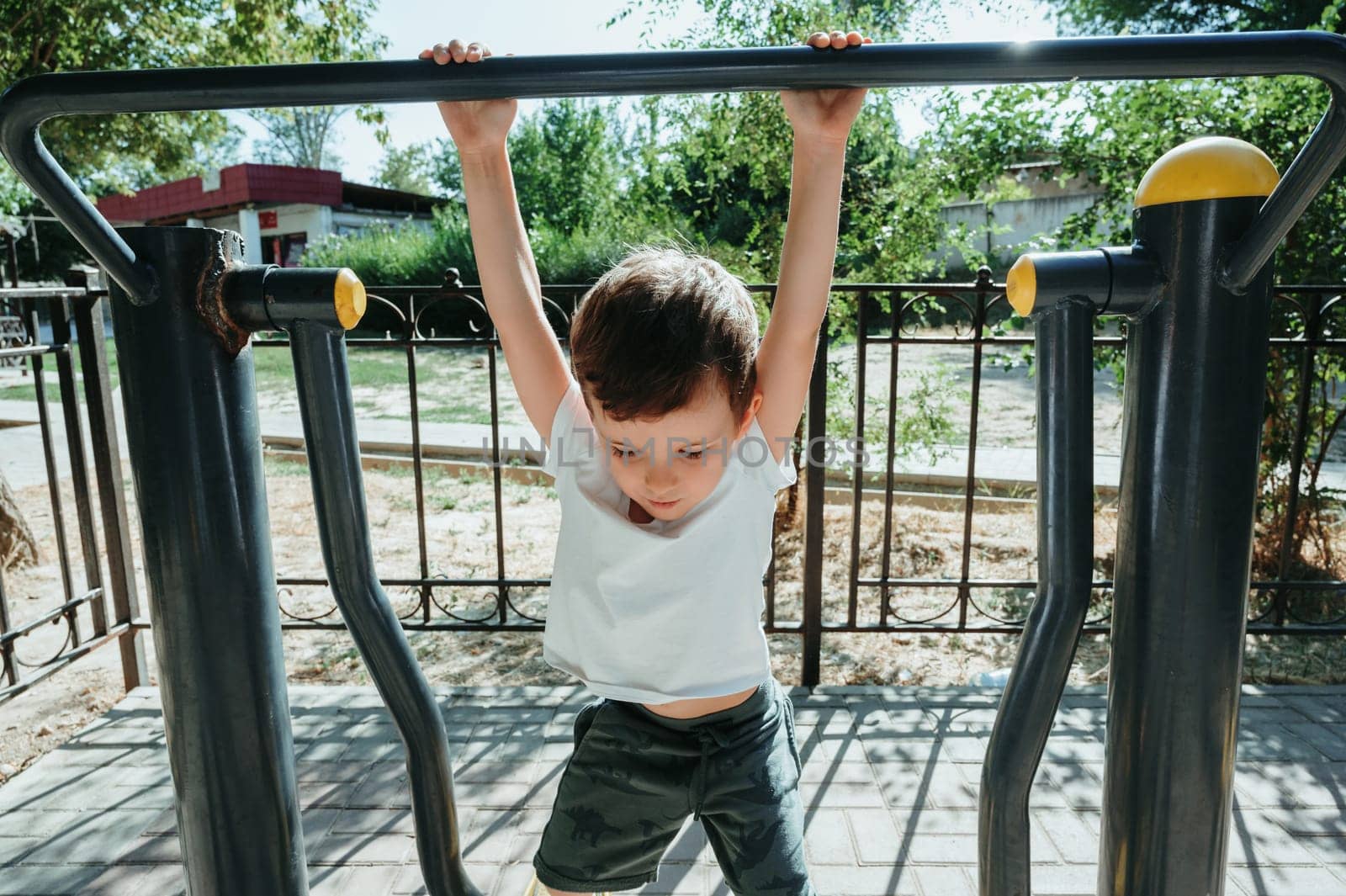 child boy playing and climbing on horizontal bars on the playground in summer