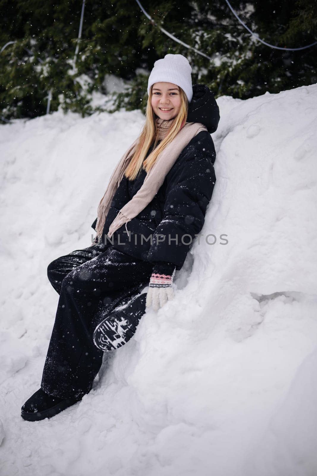 Portrait of a teenage girl sitting in a snowdrift in winter