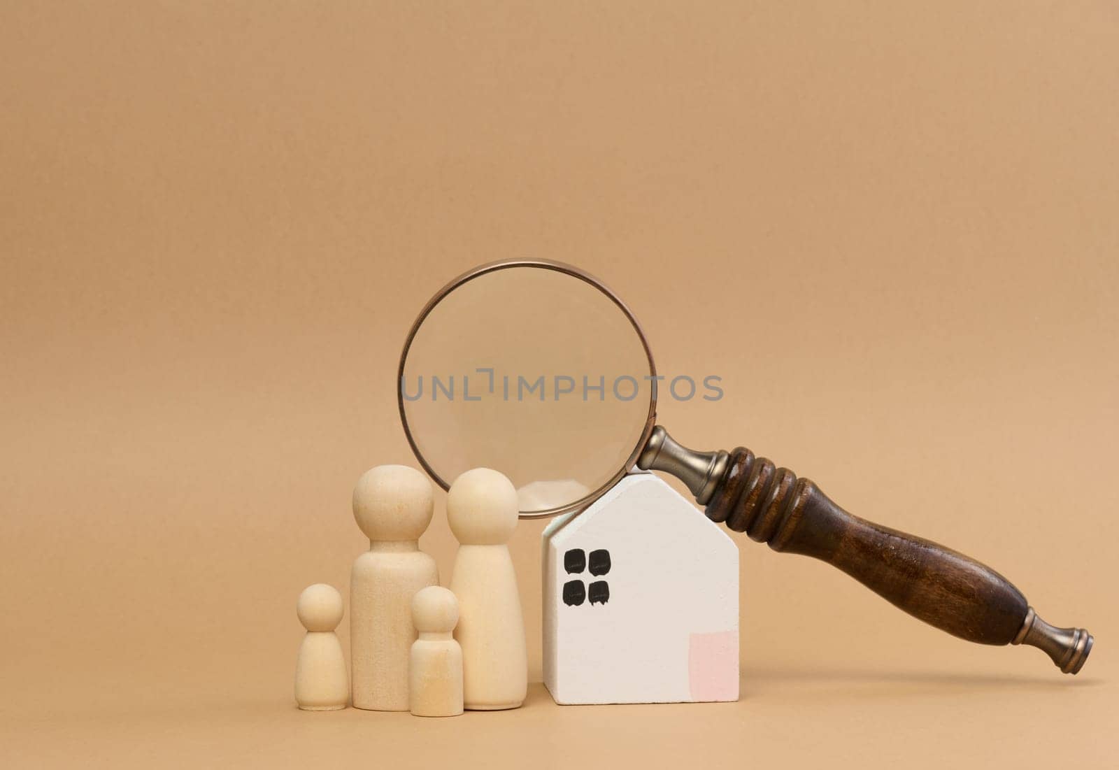 Magnifying glass and a family of wooden figures on the background of a house by ndanko