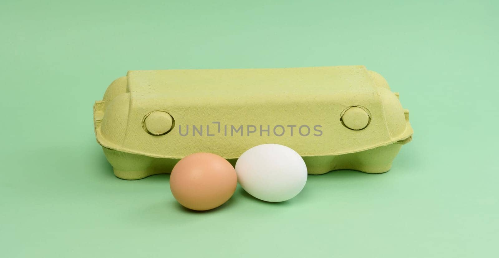 Two chicken eggs in a paper box on a green background, close up