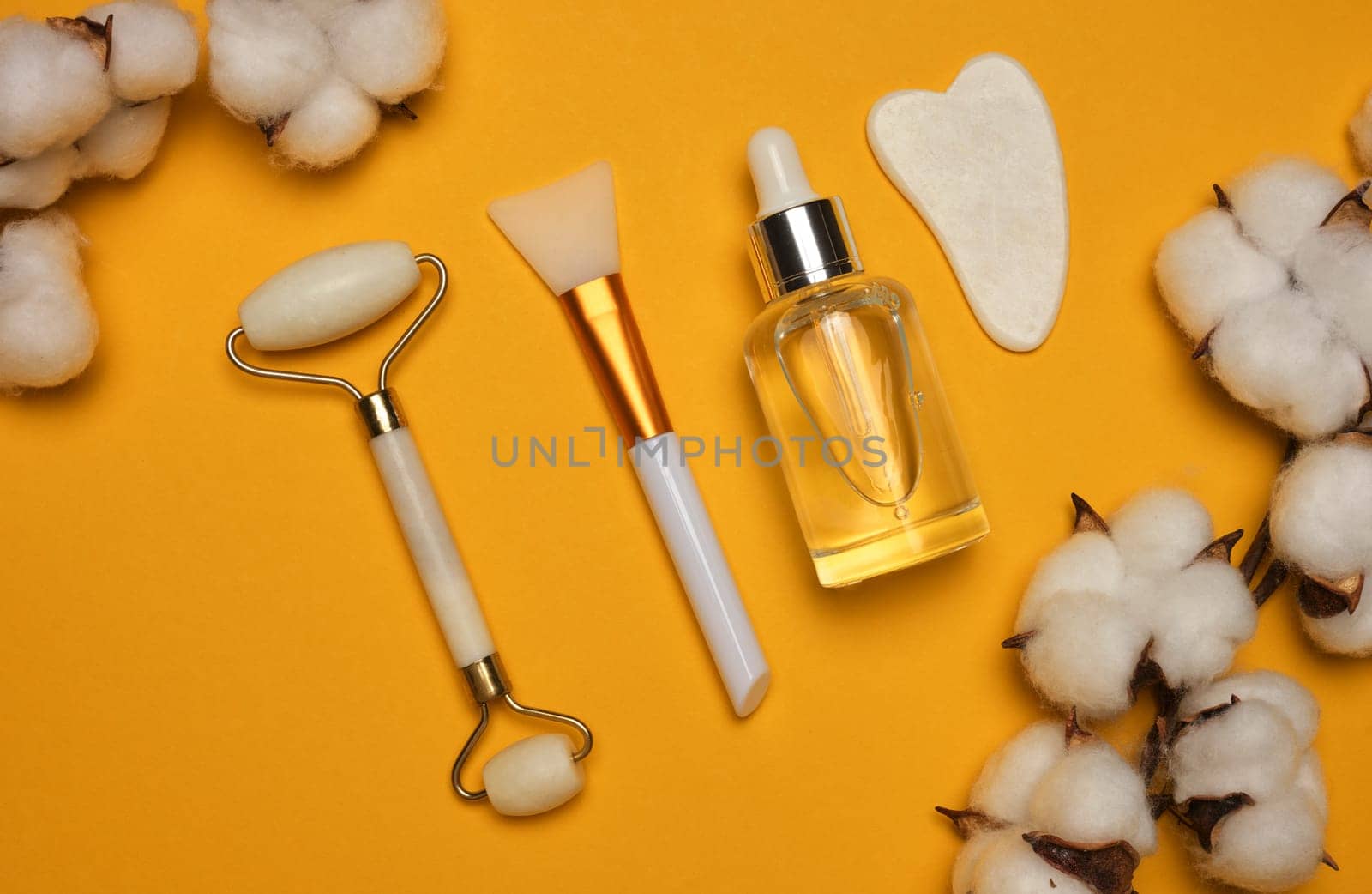 White transparent glass bottle with pipette and roller massager jade on a yellow background, top view