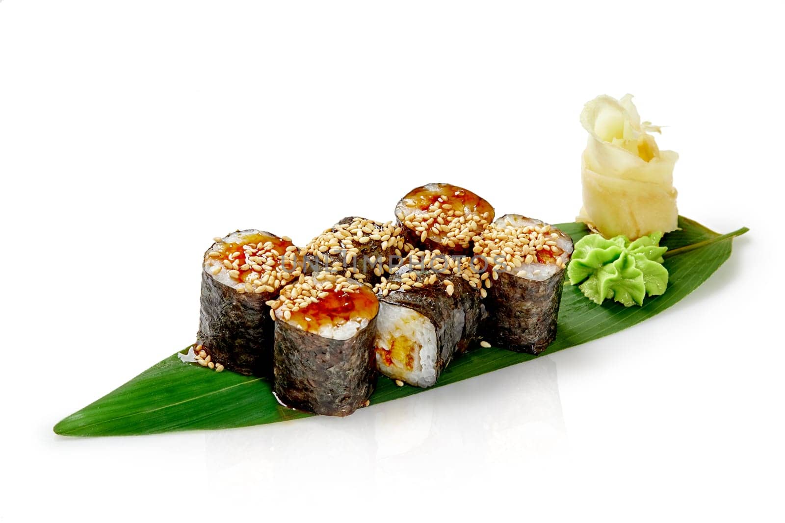 Classic maki sushi rolls with eel wrapped in rice and nori drizzled with unagi sauce and sesame, served with pickled ginger and wasabi on bamboo leaf, isolated on white. Authentic Japanese cuisine