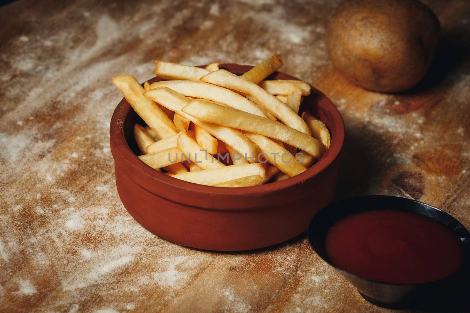 Golden French Fries in A close-up view of crispy french fries served in a bowl with a side of ketchup, ready for snacking.a Ceramic Bowl With Ketchup on a Textured Table. High quality photo