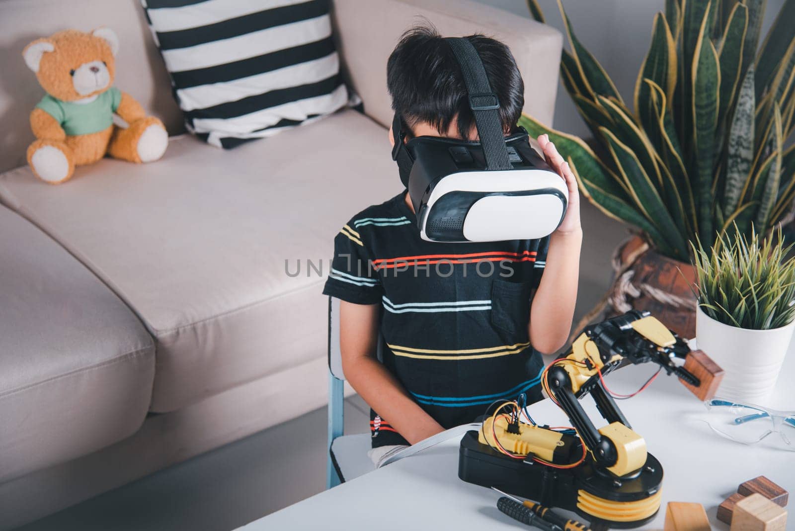 Asian kid boy using VR glasses on robotic arm in workshop by Sorapop