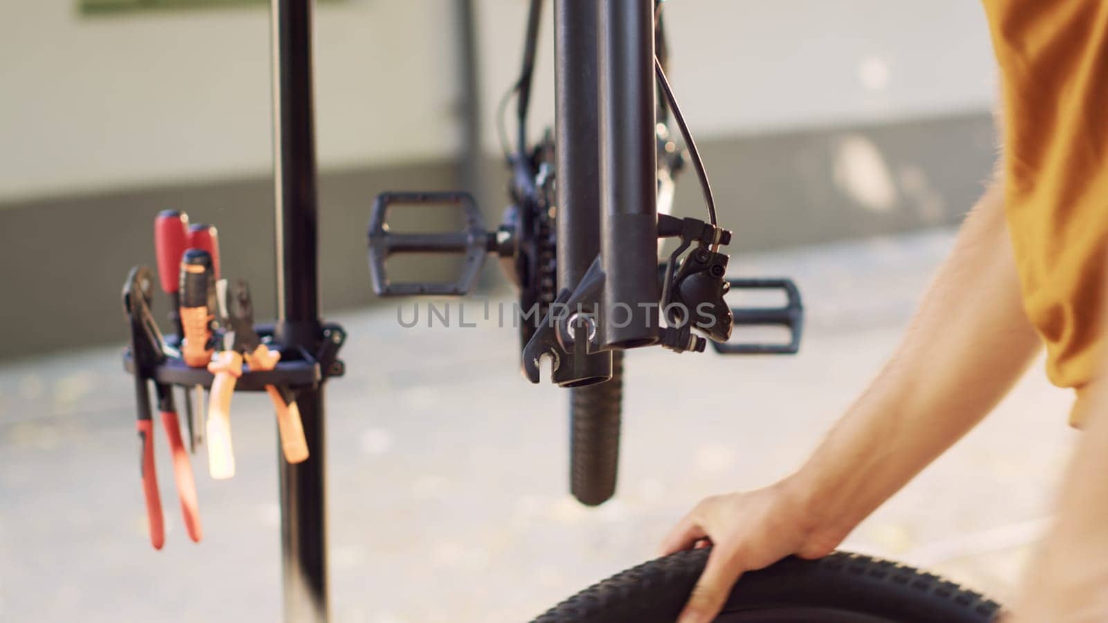 Outdoorsy caucasian man detaching bicycle wheel and adjusting handlebar in home yard. Young sports-loving male disassembling bike tire for repairing outside with professional equipment.