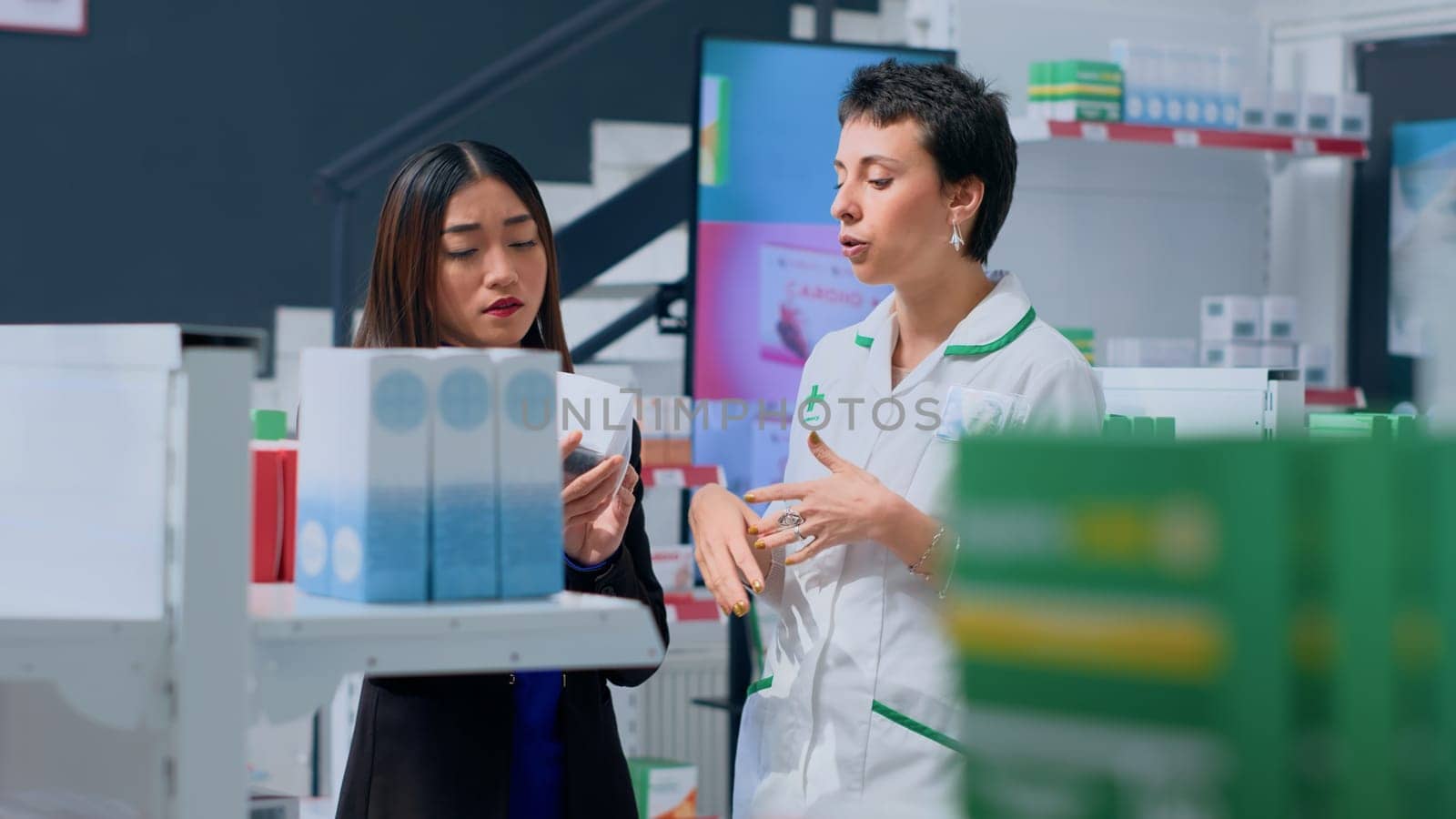 Shopper in dispensary needing prescription treatment to subdue ache, asking druggist to help her pick best medicament. Proficient pharmacologist assisting customer with product insight