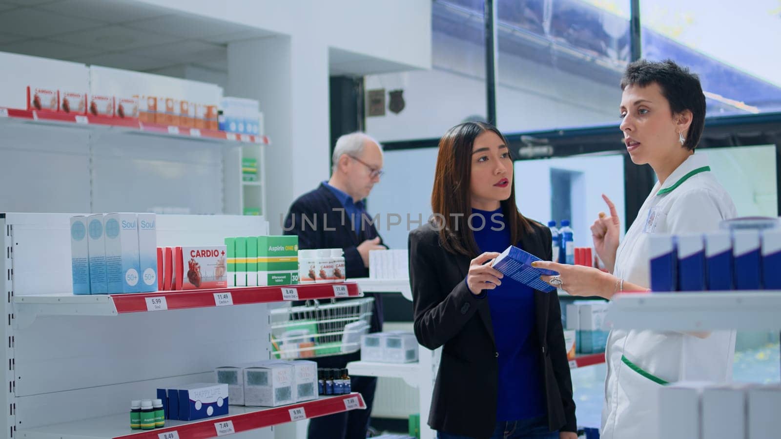 Asian woman in modern drugstore asking certified pharmacist for medical advice. Licensed druggist helping customer trying to pick best pharmaceutical product to treat sickness