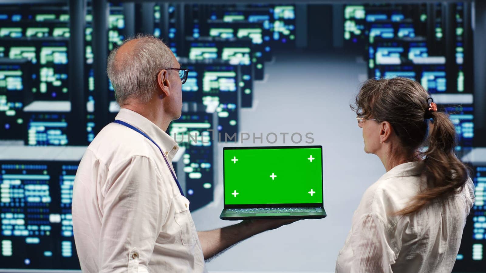 Experienced professionals looking around high tech data center, using mockup laptop to crosscheck disaster recovery plan and assess server infrastructure in need of replacement, preventing issues