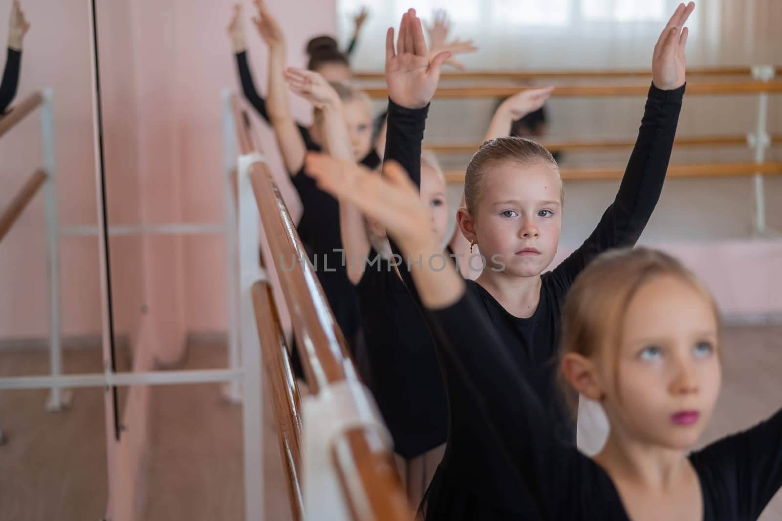 Cute little girls in black swimsuits and tutu do ballet at the barre