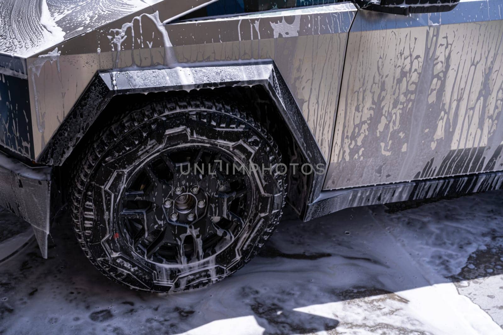 Denver, Colorado, USA-May 5, 2024-Close-up image of a Tesla Cybertruck being washed, showcasing the vehicle angular design and rugged tires. Water and soap suds cover the metallic surface, highlighting the unique texture and design elements of the electric truck.