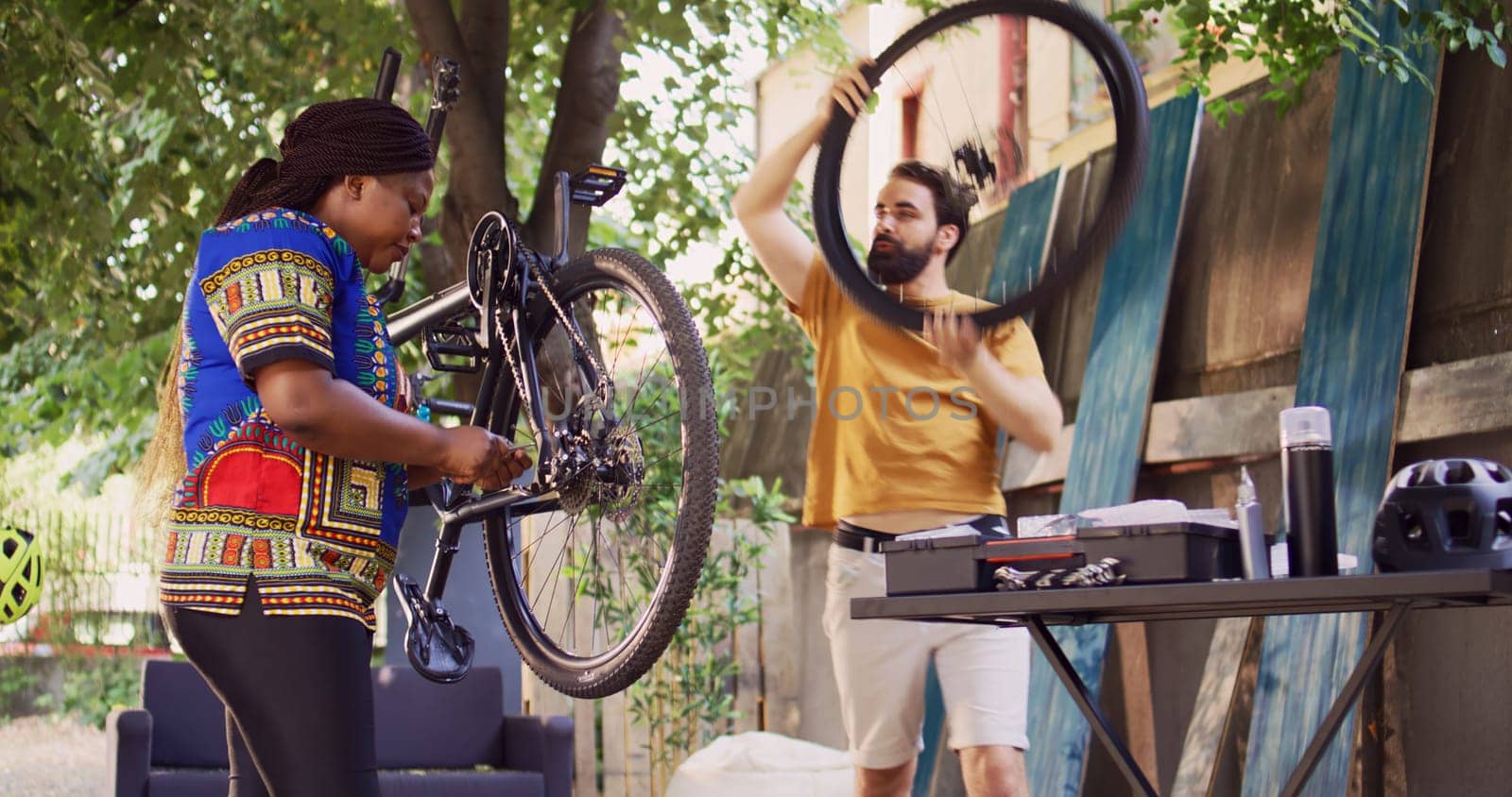 Young multiracial pair fixes broken bike with professional equipments. Caucasian man dismantling wheel while black woman adjusts chains and pedals for yearly bicycle repair and maintenance.