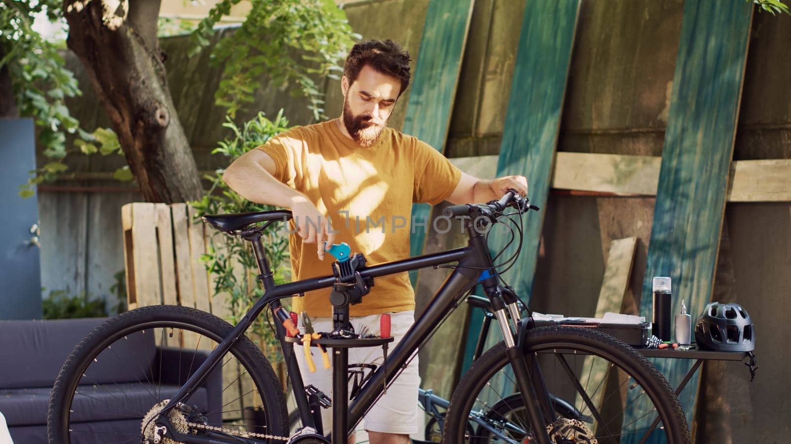Healthy active male cyclist carefully carrying and positioning bicycle for maintenance. Youthful caucasian man fixing bike damages in backyard with specialized repair-stand and tools.