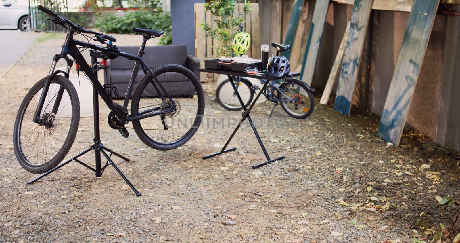 View of modern damaged bikes placed and secured in home yard ready for maintenance with professional equipment. Aerial shot of bicycle on repair-stand next to specialized toolbox outdoor.