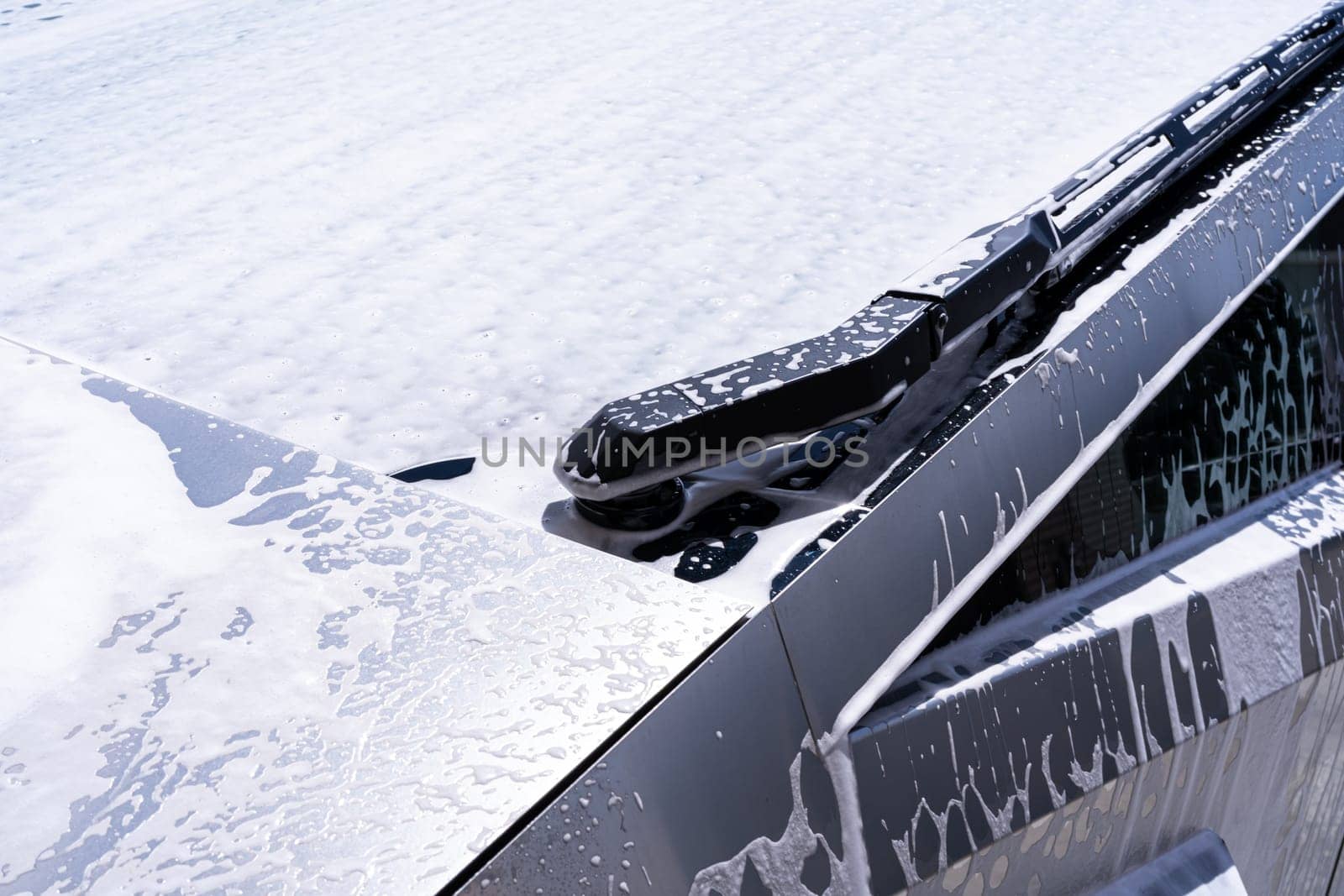 Denver, Colorado, USA-May 5, 2024-This image captures a close-up view of a Tesla Cybertruck hood and windshield wipers covered in soap suds during a car wash. The photograph highlights the sleek, reflective surface of the electric vehicle as it undergoes cleaning.