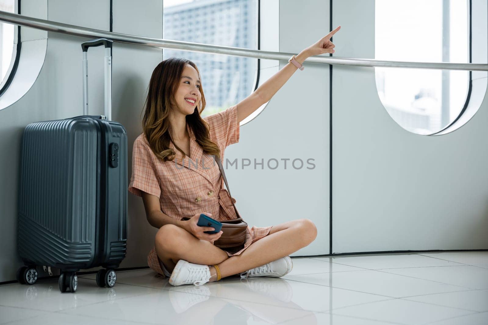 interested and curious woman sitting on the floor at the airport with her suitcase by Sorapop