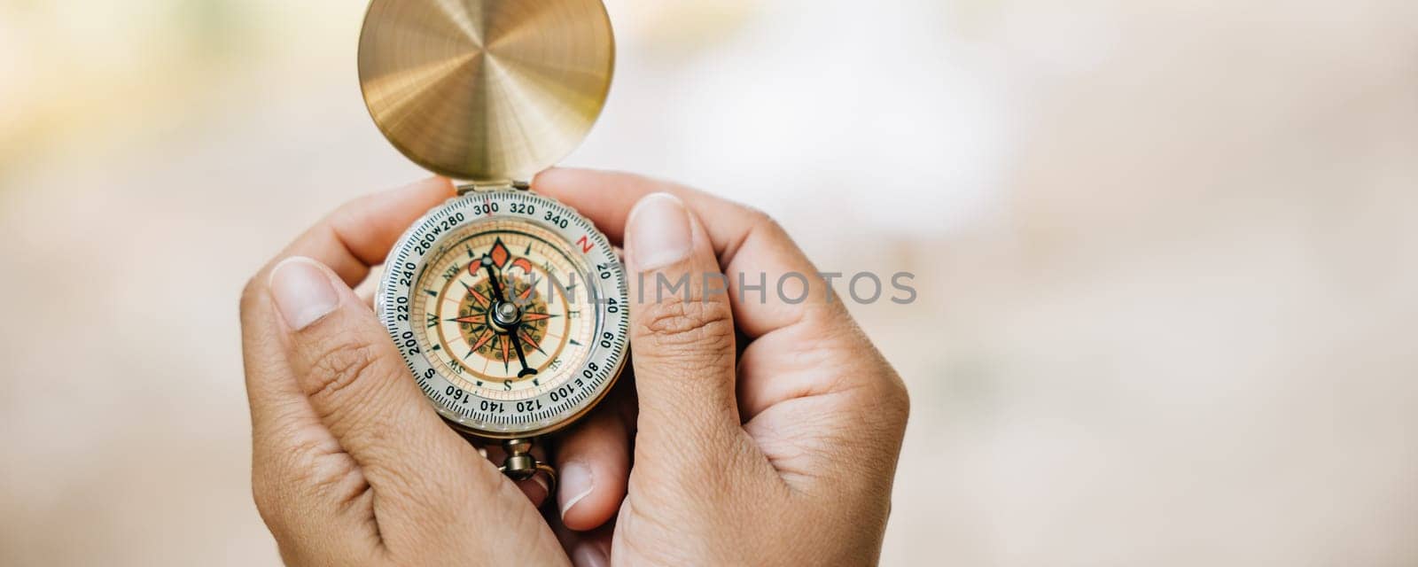 Surrounded by the beauty of nature a woman's hand grips a compass in a tranquil forest and lake setting. The image symbolizes guidance and the exciting spirit of exploration amidst the outdoors. by Sorapop