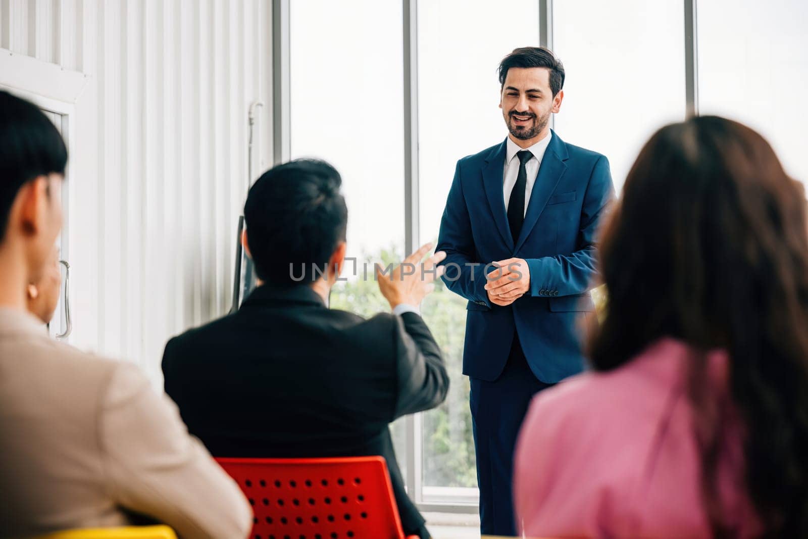 In a meeting room, business leaders present their insights, while a diverse audience of colleagues attentively listens. This image signifies the success of teamwork and collaborative discussions. by Sorapop