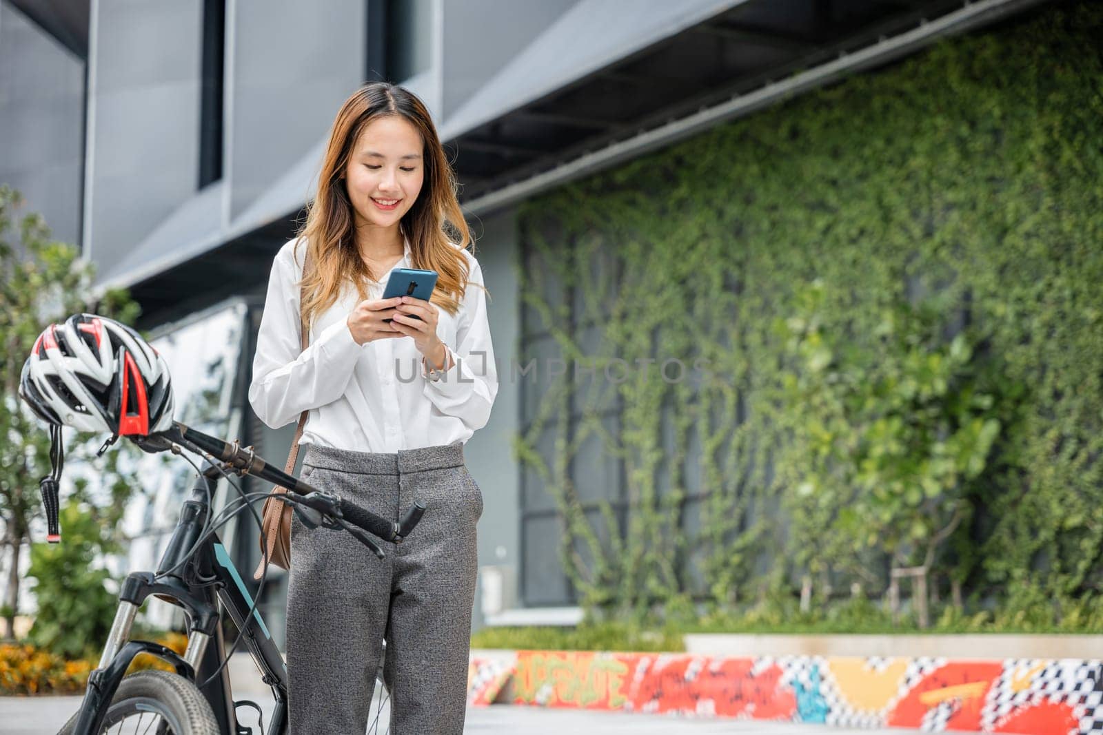 A young businesswoman smiling and holding her smartphone enjoys a bike ride through the city. Her ability to blend work and fun is a testament to the modern concept of work-life balance.
