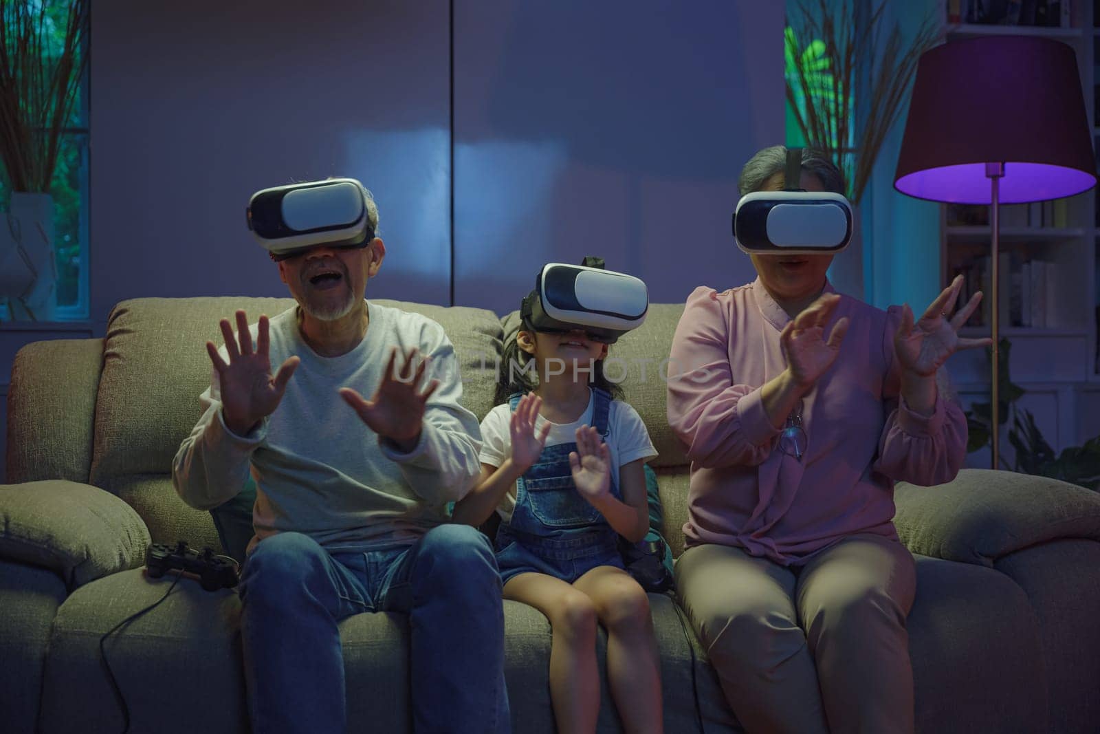 Asian elderly with child play VR video game, family entertainment, granddaughter and grandparents playing together exciting interesting video games using virtual reality headsets living room at home