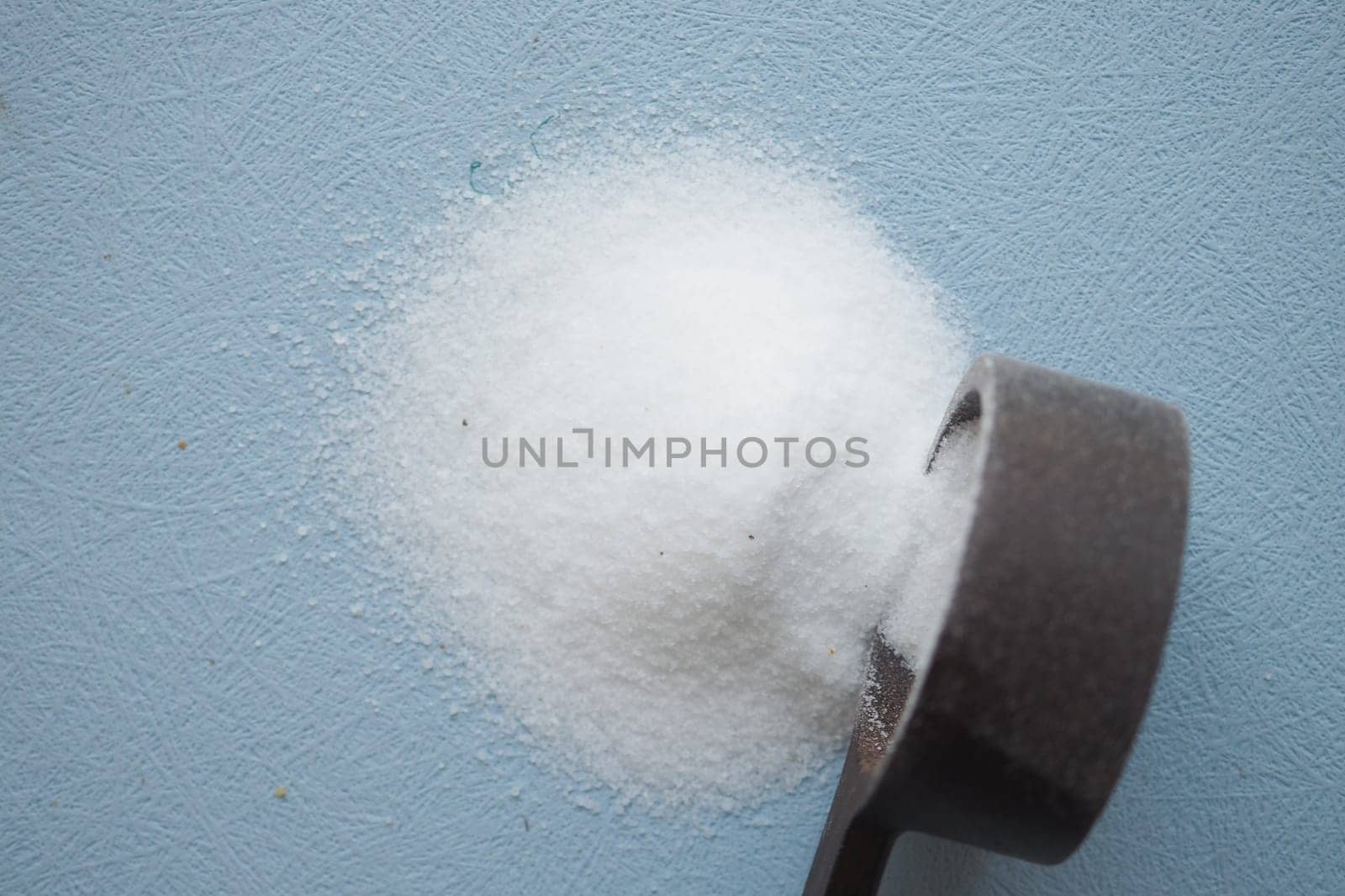 top view of white salt and a wooden spoon on a light blue background ,