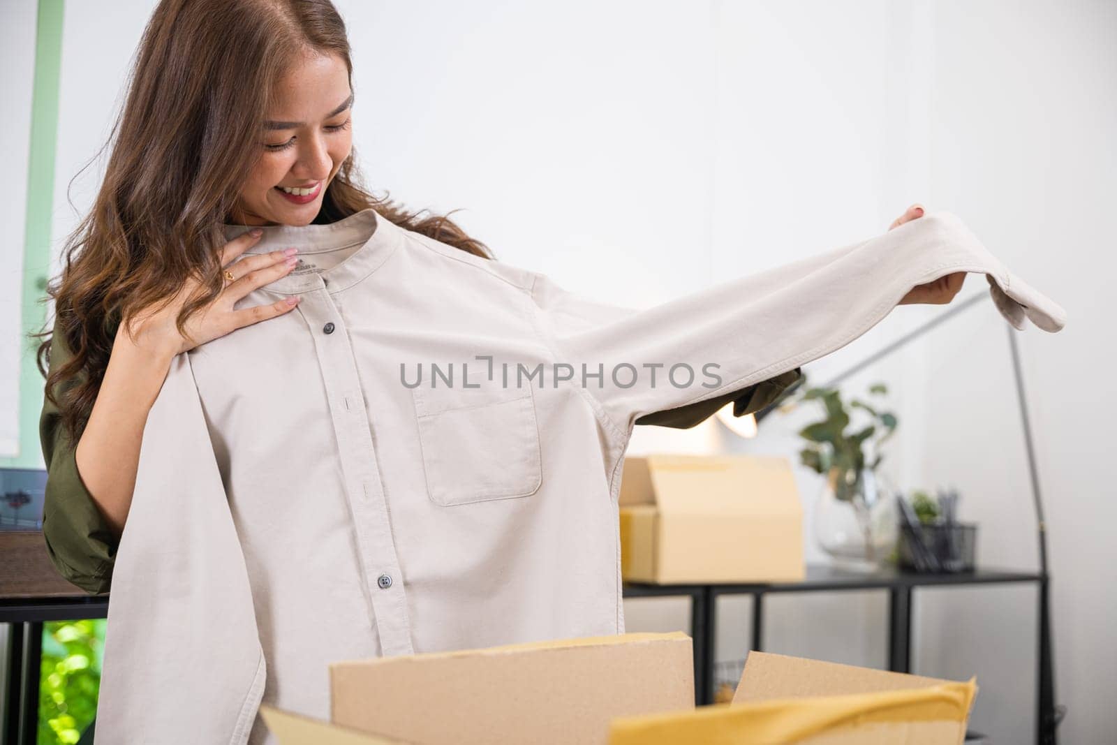 Happy Asian woman customer opening box and shirt against body new clothes, Excited smiling female shopper unboxing cardboard box package, shopping online from home, delivery shipping concept