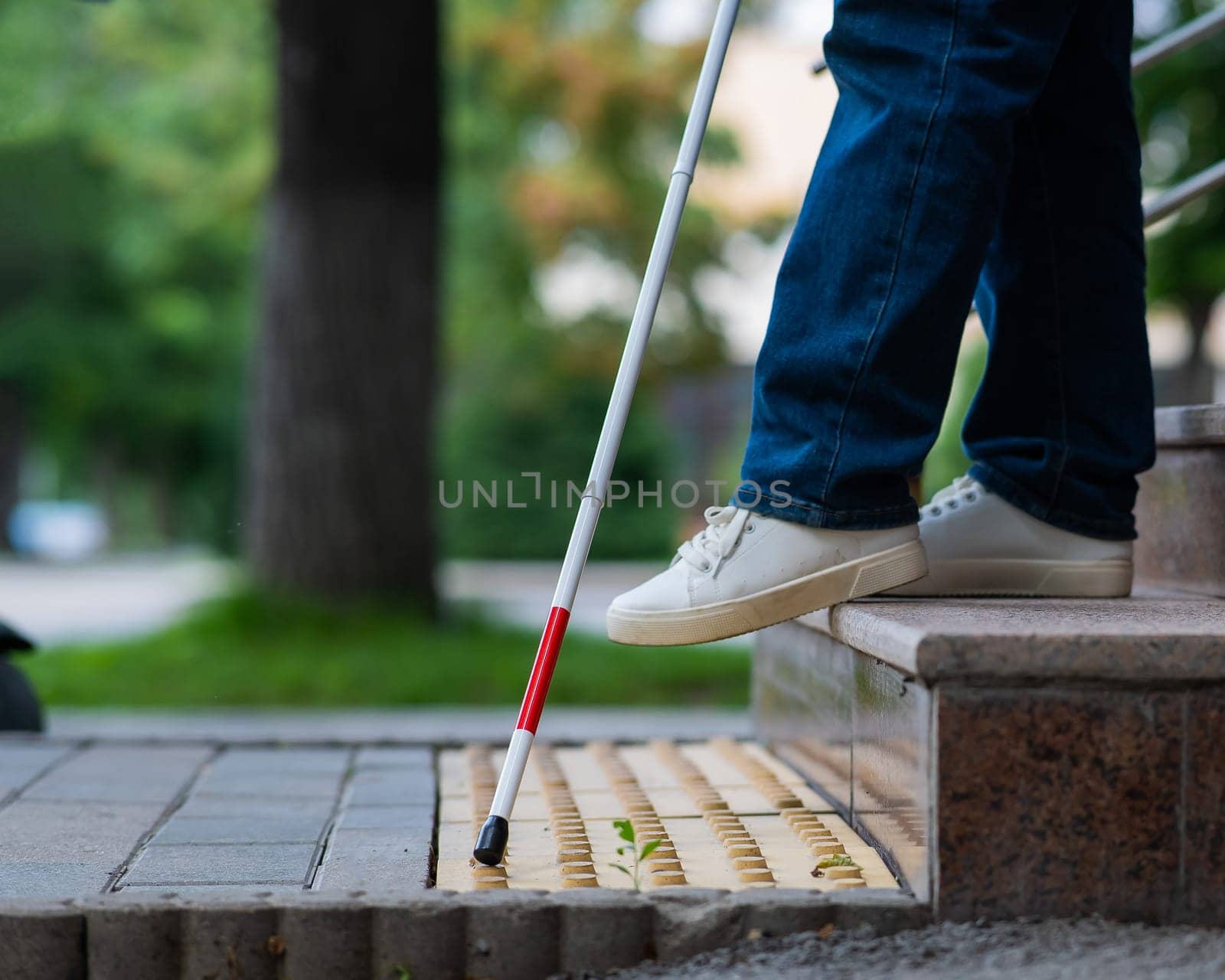 Close-up of female foot, walking stick and tactile tiles. Blind woman walking down stairs using a cane. by mrwed54