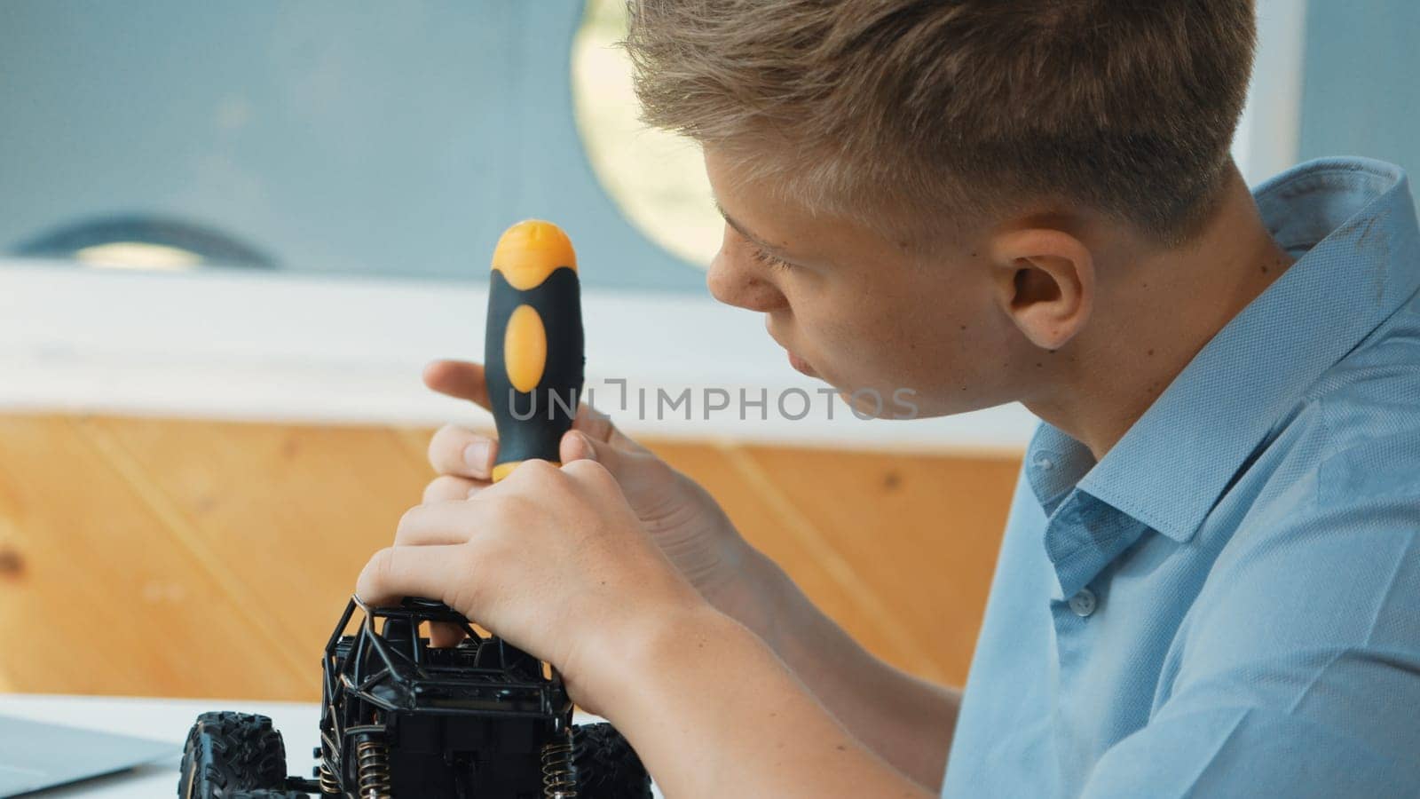 Close up of young student tighten the nut by using screwdriver. Caucasian teenager repairing or fixing car model while inspect robotic machine construction at STEM technology class. Edification.