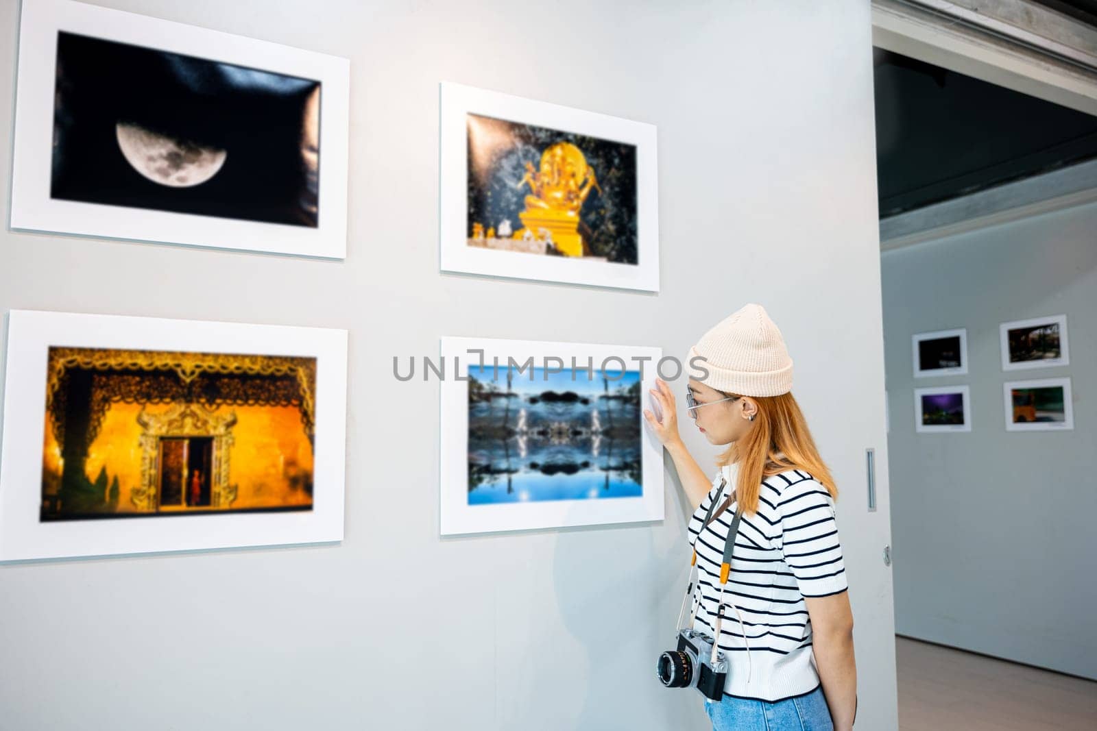 Asian woman hold camera at art gallery collection in front framed paintings pictures on wall and looking, Photographer visit at photo frame to leaning against at show exhibit artwork gallery picture