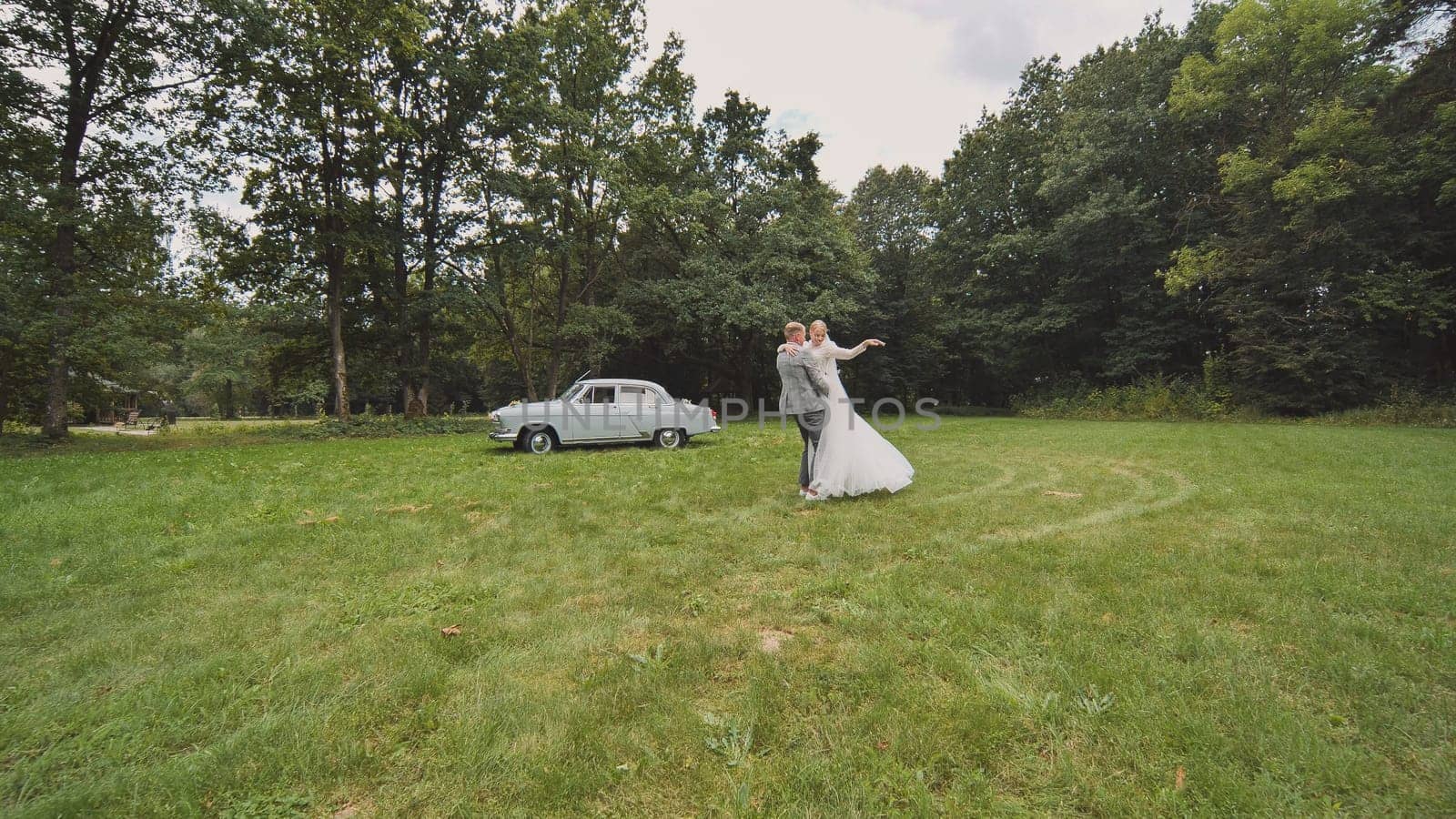 Bride and groom twirling in the background of a retro automobile