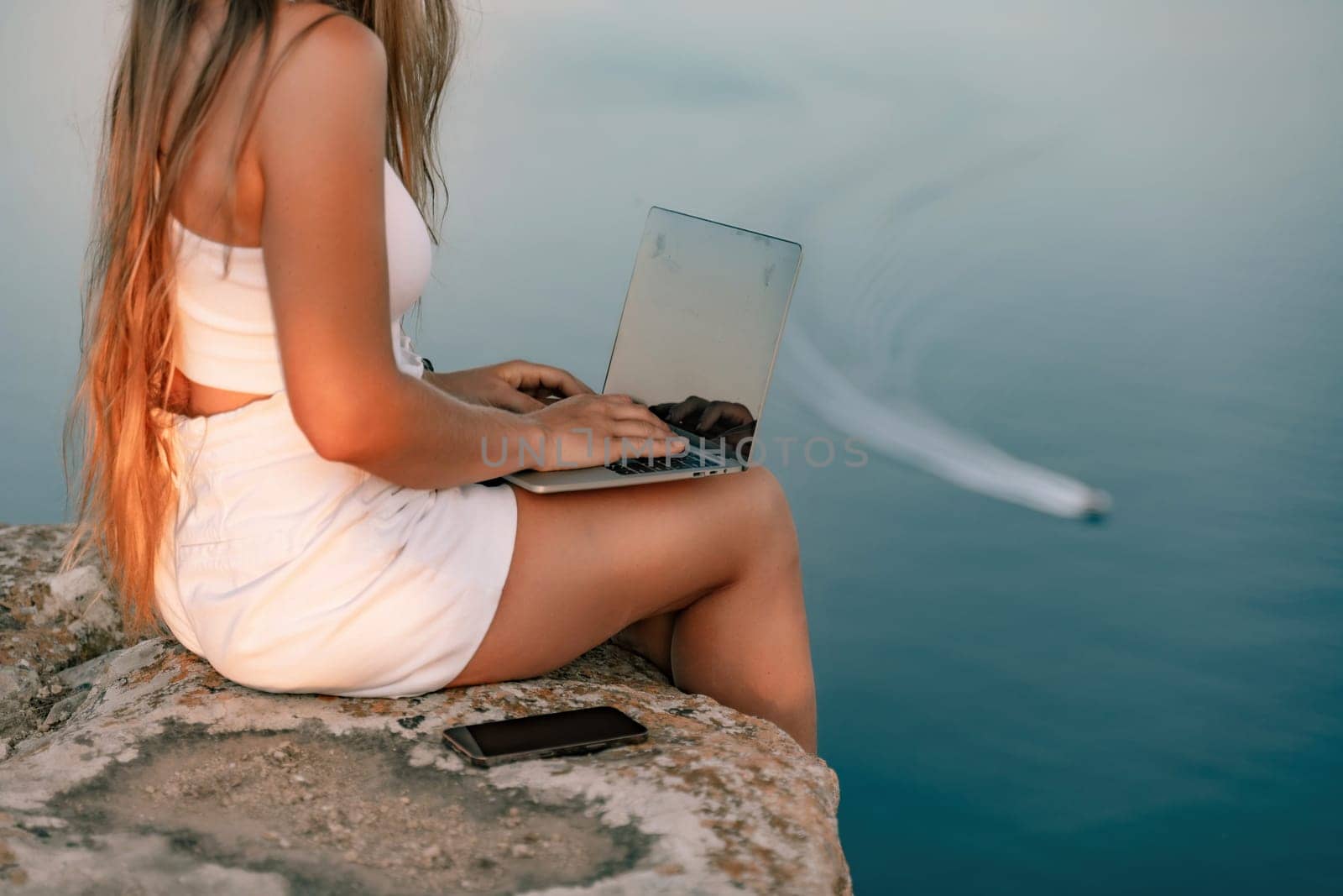 Freelance women sea working on the computer. Good looking middle aged woman typing on a laptop keyboard outdoors with a beautiful sea view. The concept of remote work