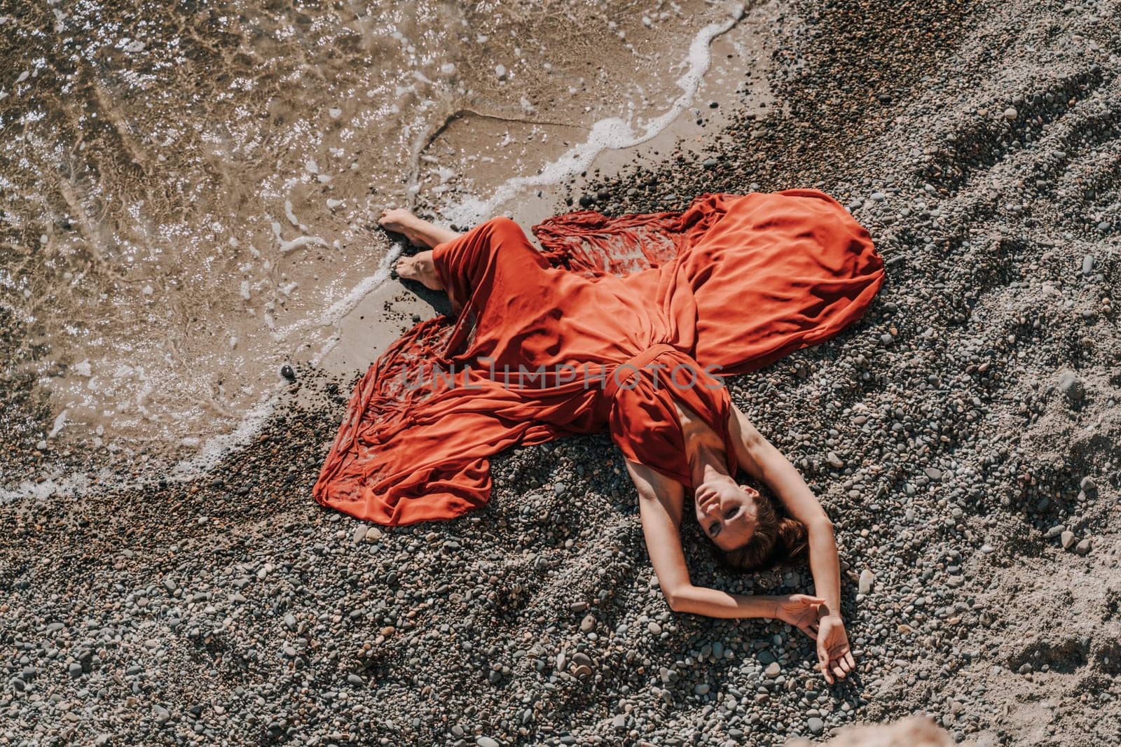 Woman red dress sea. Female dancer in a long red dress posing on a beach with rocks on sunny day by Matiunina