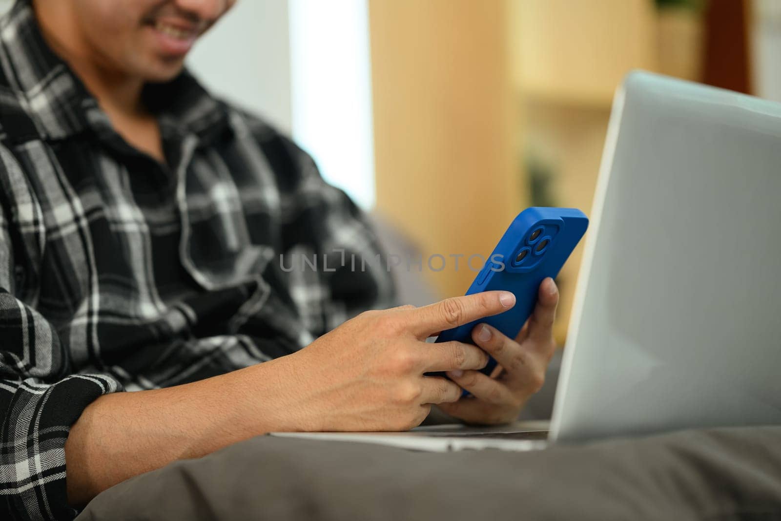 Smiling young man using smartphone, chatting to colleagues and clients over the internet.