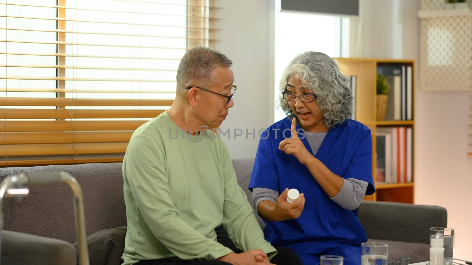Smiling female general practitioner explaining medicine dosage to senior patient during home visit.