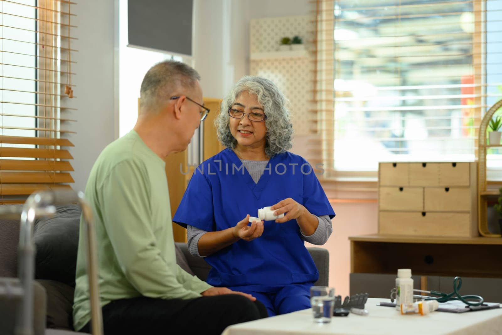Smiling female general practitioner explaining medicine dosage to senior patient during home visit by prathanchorruangsak