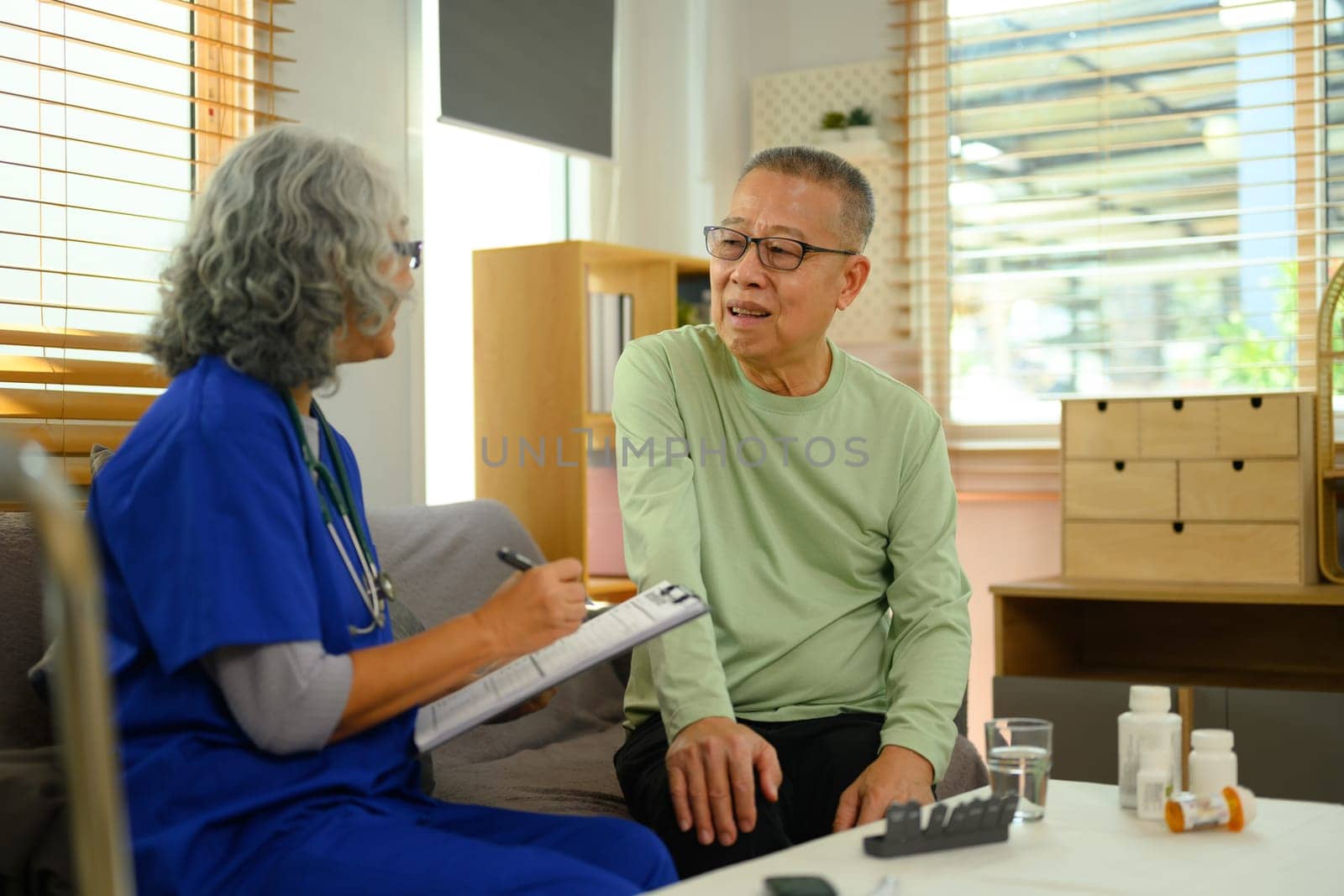 Friendly doctor and senior patient talking during health check up at home. Health care concept by prathanchorruangsak