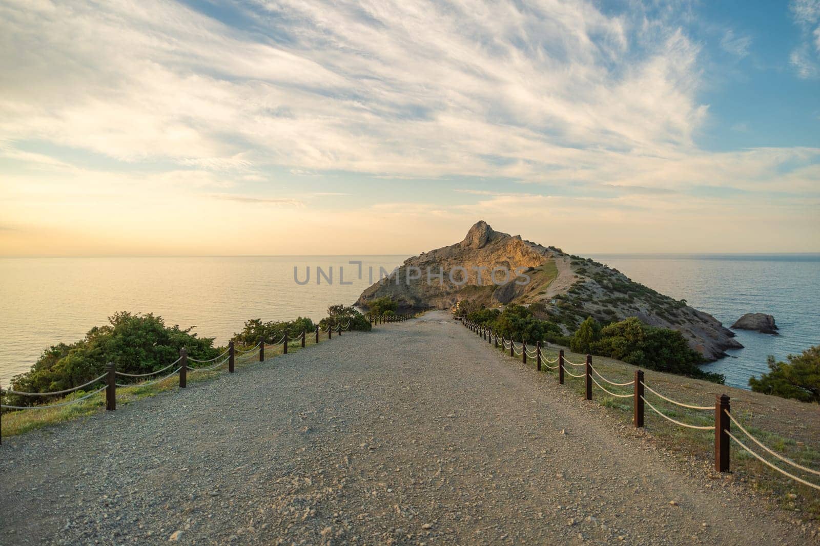 A rocky beach with a long road leading to a cliff. The road is lined with wooden posts and the sky is cloudy