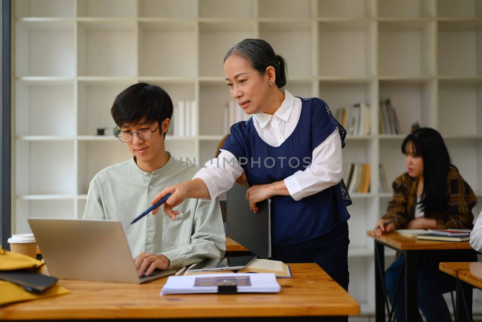 Shot of mature professor walking and checking student homework in the classroom.