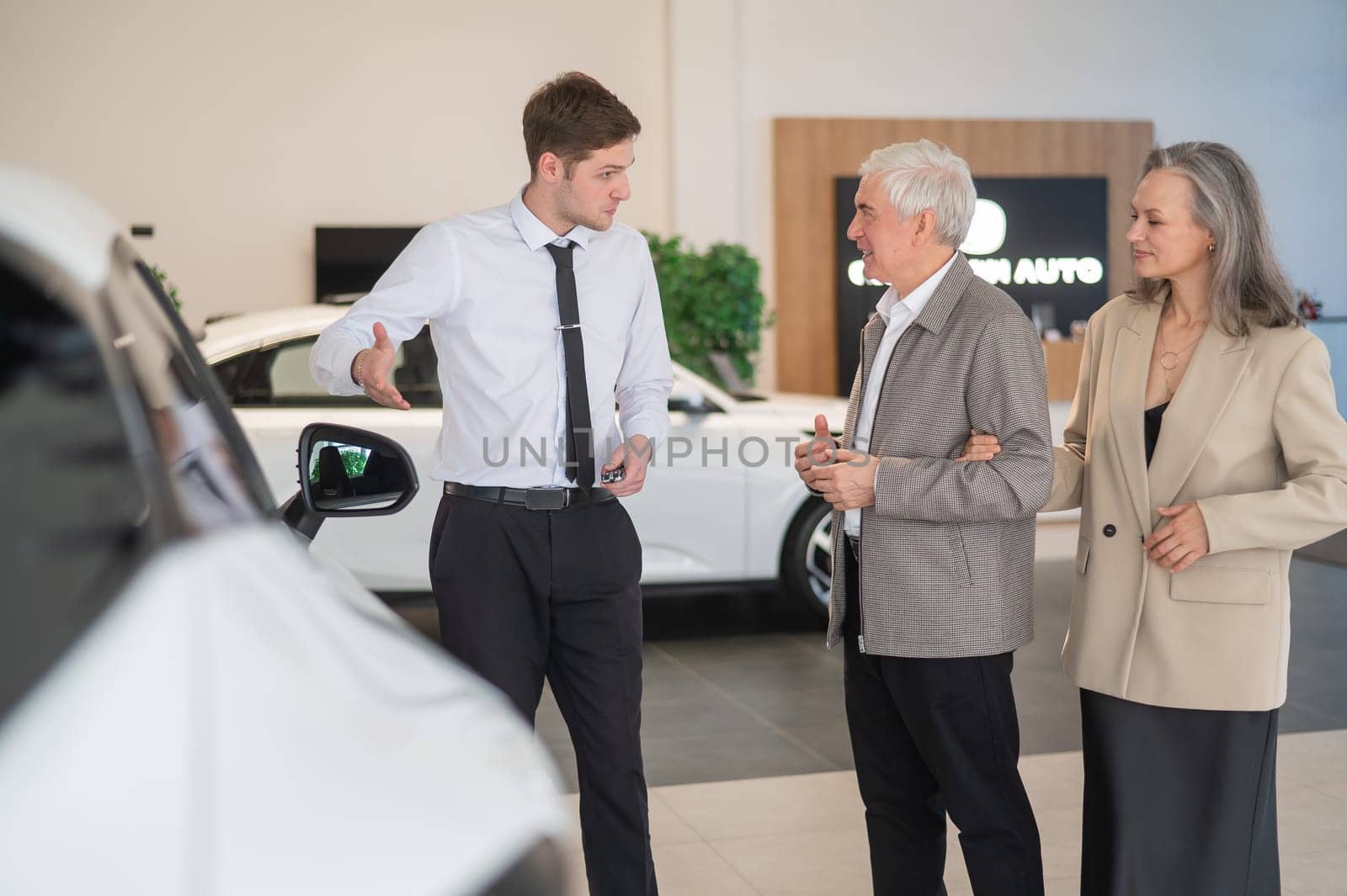 A salesman in a car dealership shows a car to a mature married couple