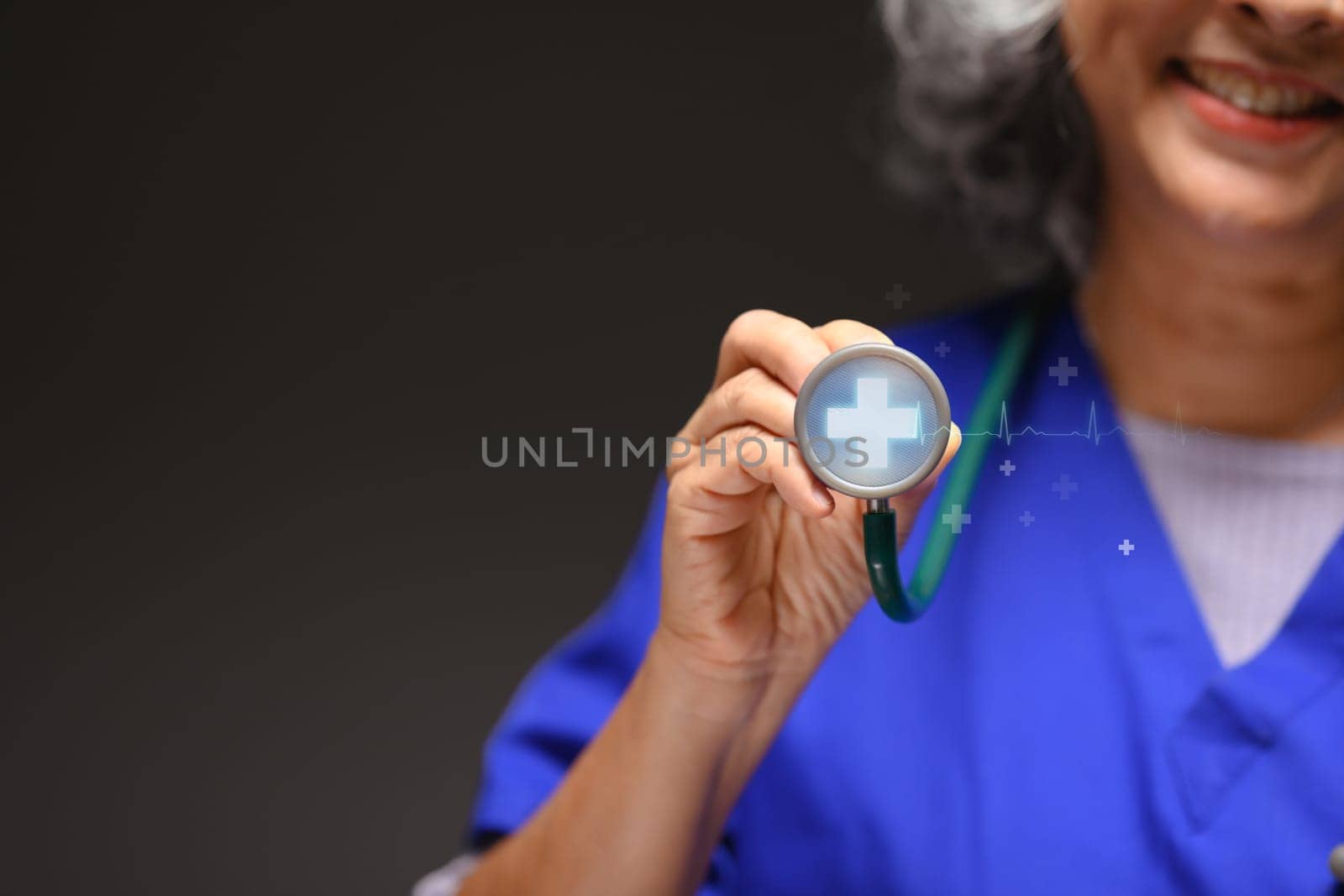Smiling mature doctor holding stethoscope with modern medical plus sign. Medical innovative technology concept.