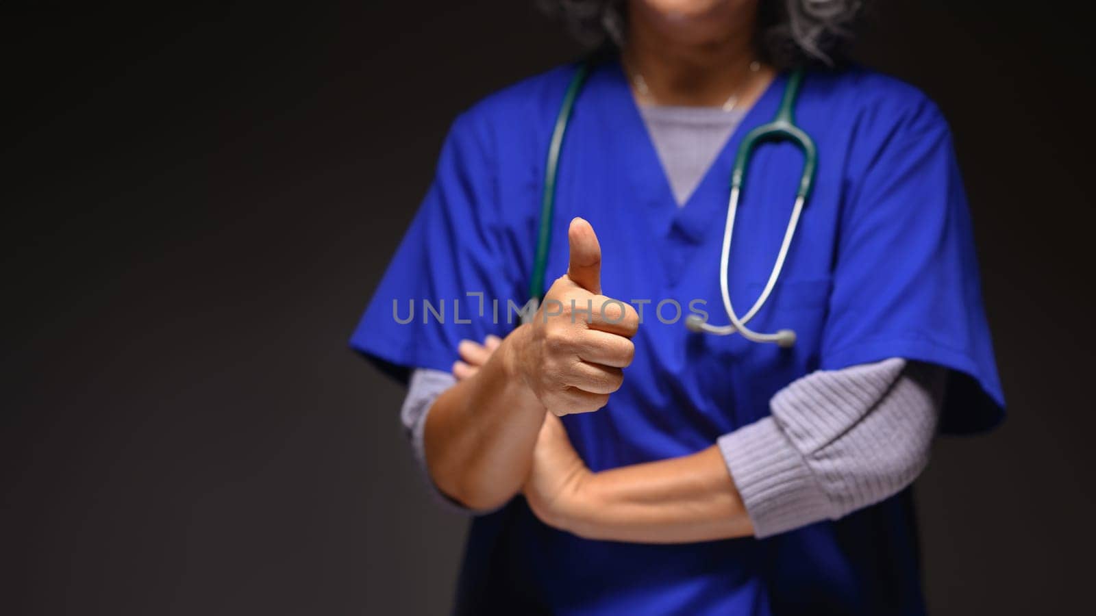 Mature doctor in medical uniform showing thumbs up over black background. Health care concept.