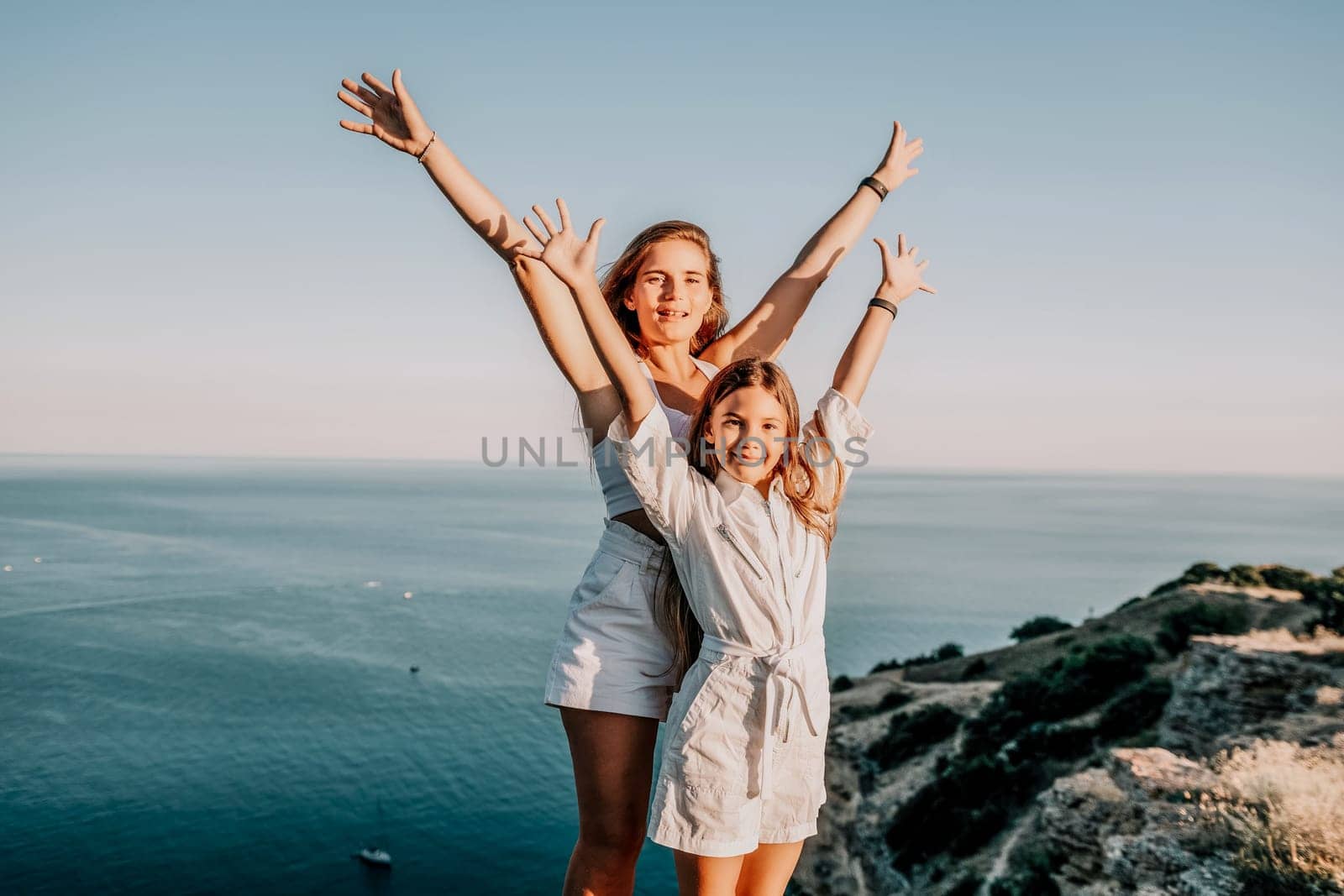 Close up portrait of mom and her teenage daughter hugging and smiling together over sunset sea view. Beautiful woman relaxing with her child.