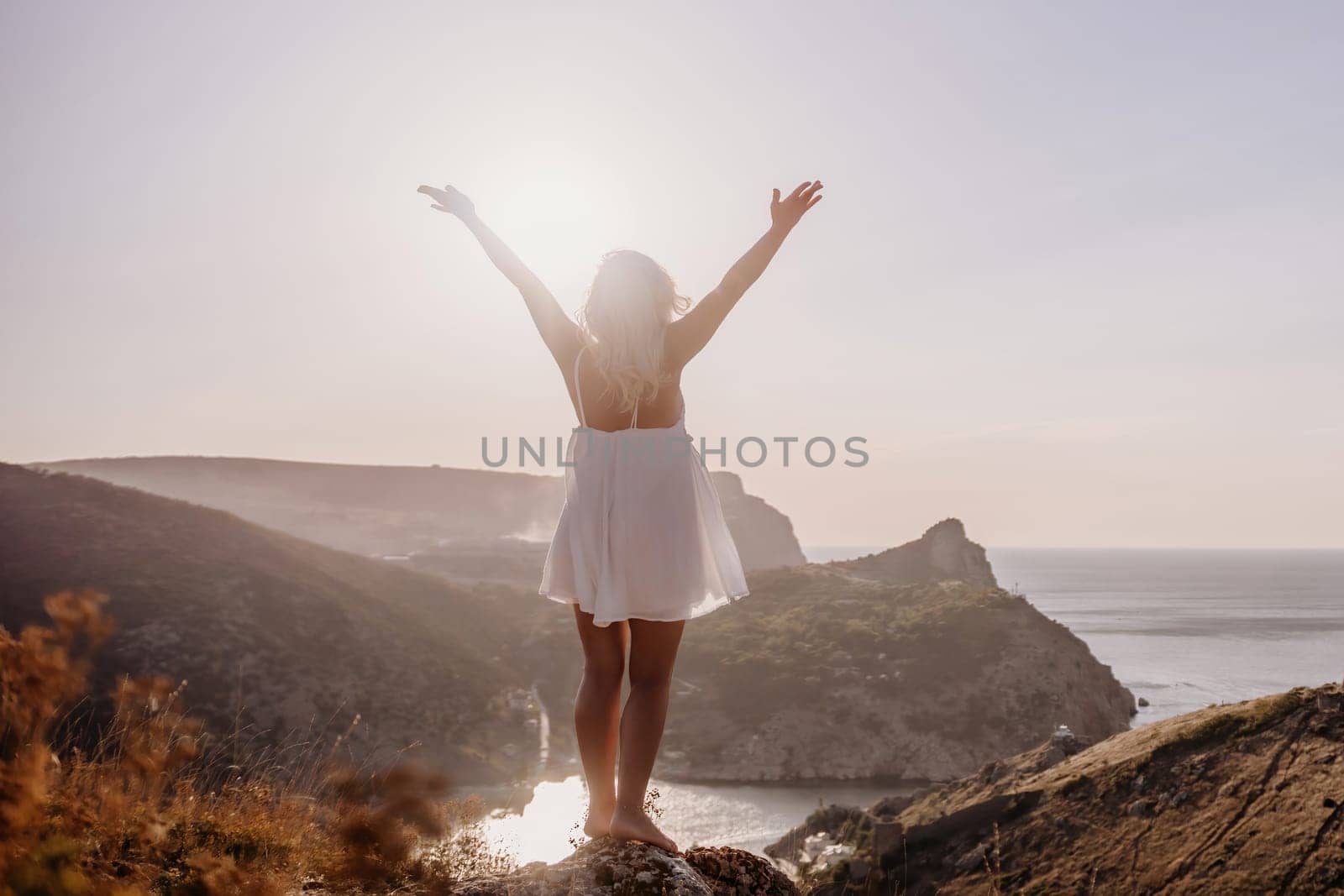 A woman is standing on a hill overlooking a body of water. She is wearing a white dress and she is happy