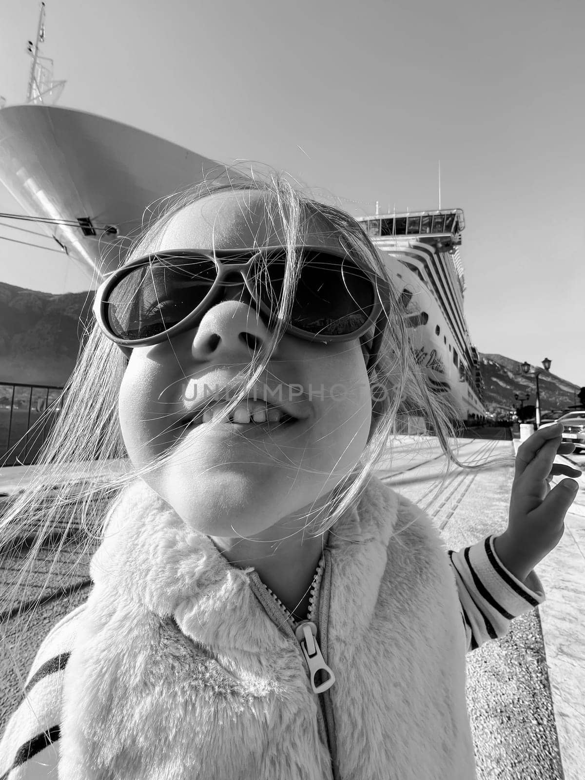 Little girl in sunglasses on the background of a large boat. Black and white photo. High quality photo
