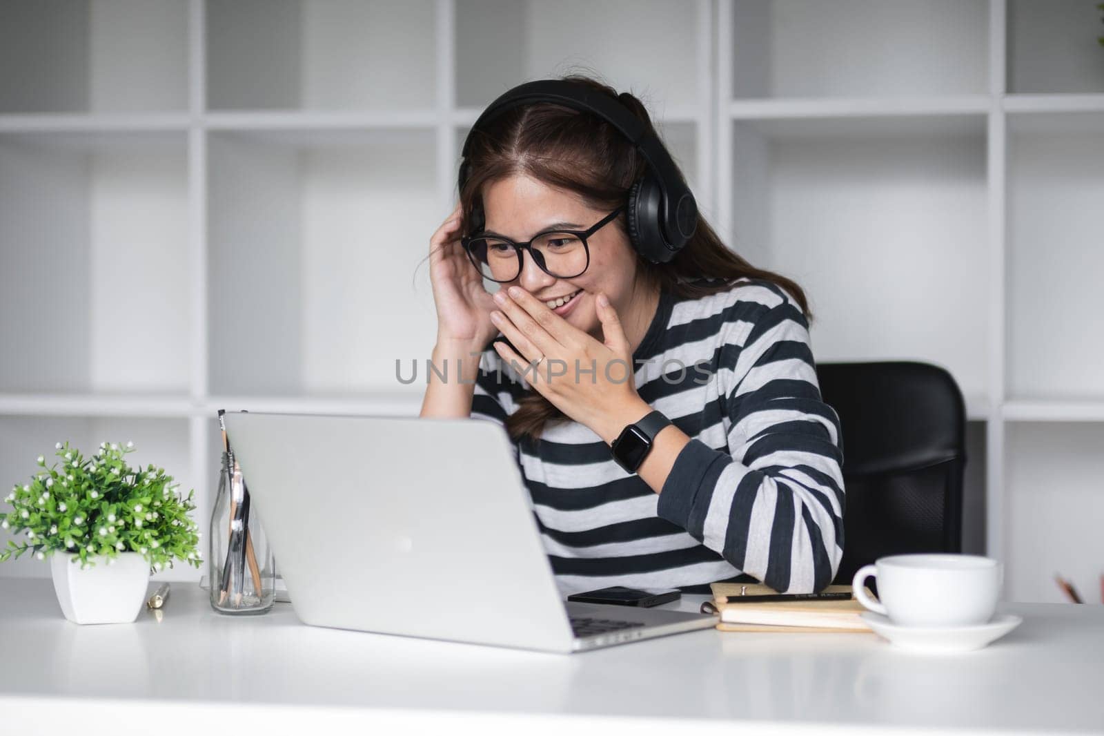 Beautiful accountant wears headphone to chat with coworkers via online call program on work from home day.