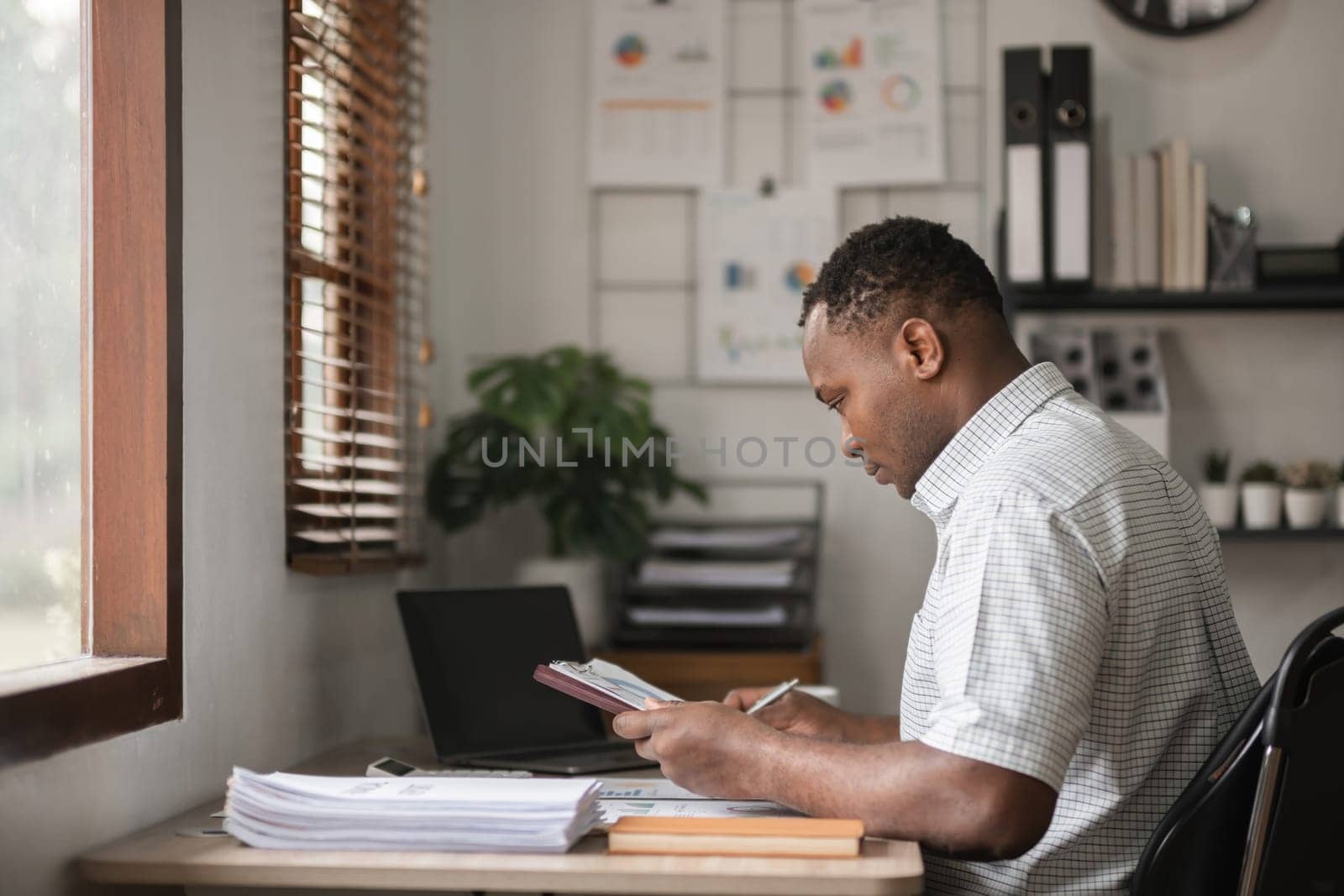 African American businessman working on paperwork, searching for information with laptop at home office.