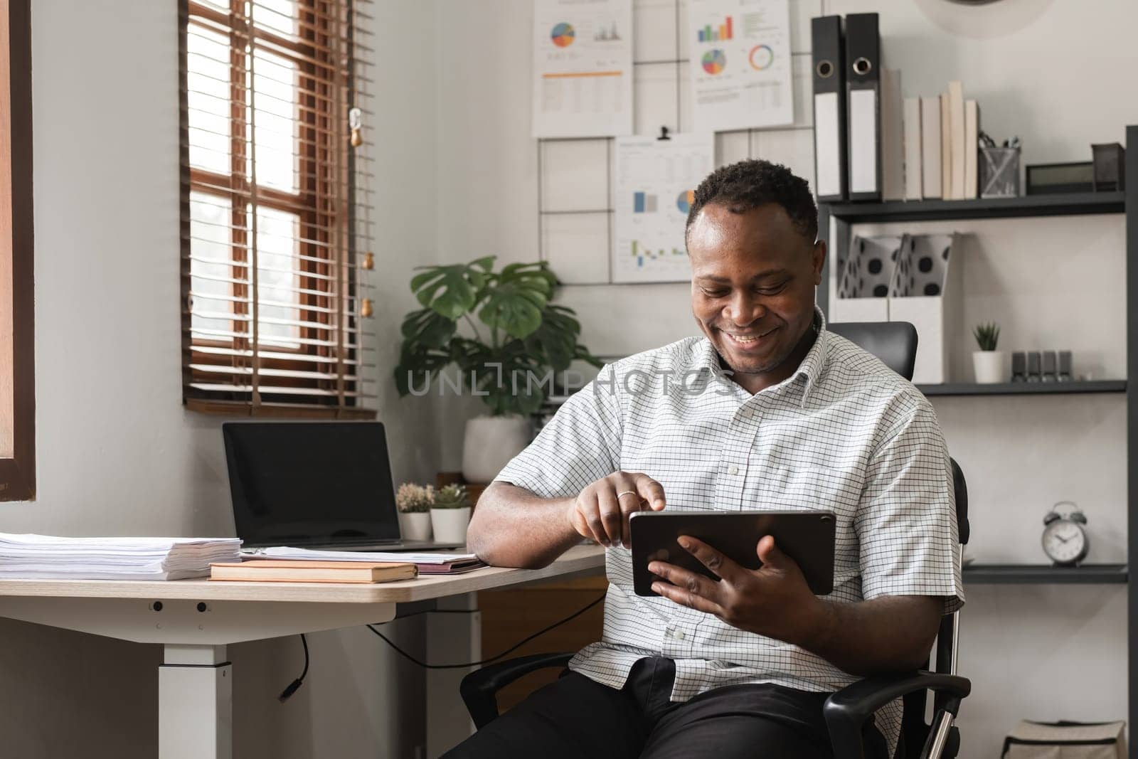 African American businessman working on paperwork, searching for information with laptop at home office by wichayada