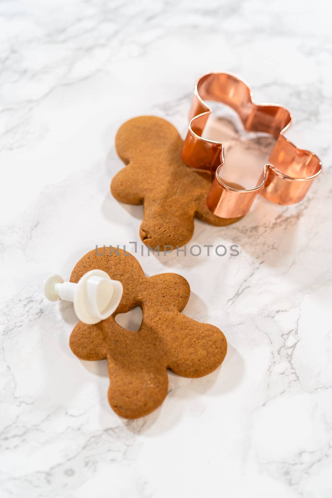 Gingerbread cookies, including a gingerbread man with a heart-shaped cutout, rest on a rustic metal tray against a marble countertop.