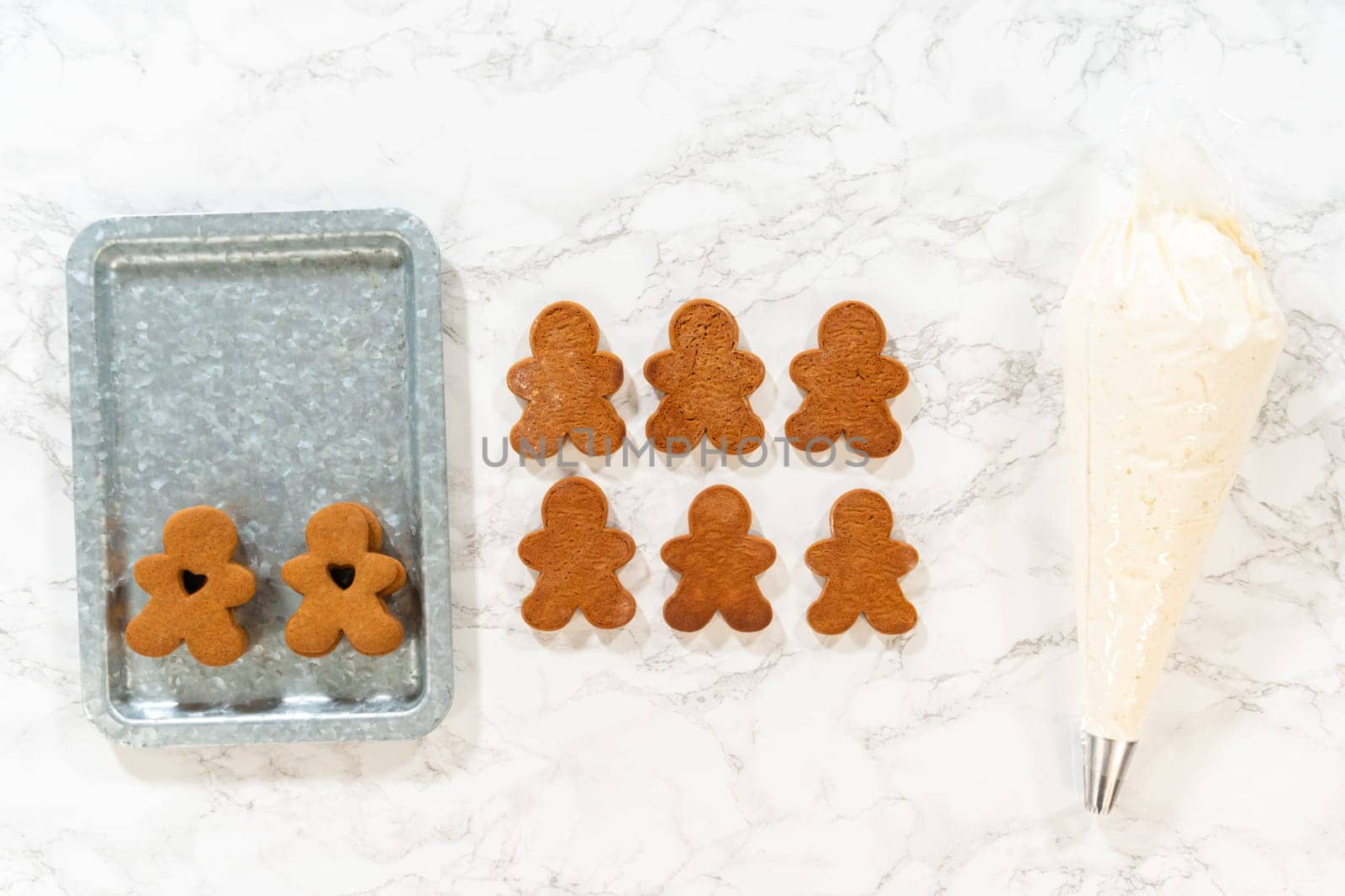 Flat lay. Gingerbread cookies await their second halves on a marble surface, each meticulously piped with buttercream to craft delightful sandwich treats. The precision of the piping adds a festive touch.